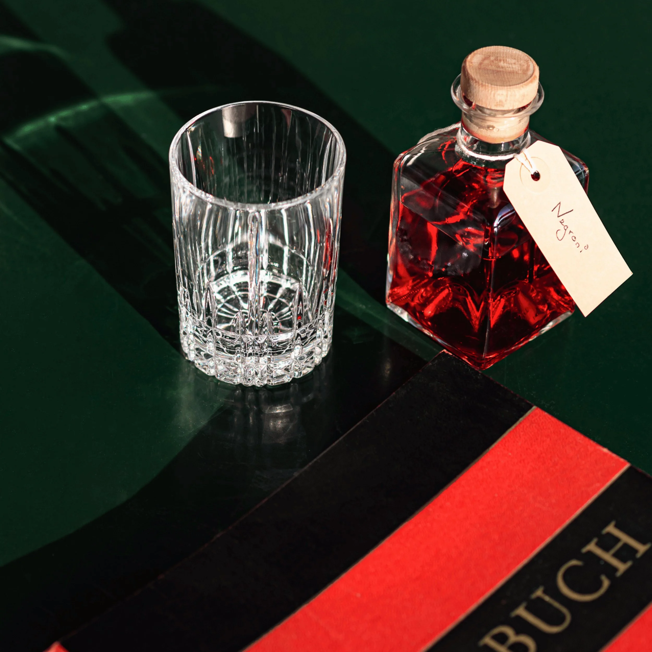 Vetro strutturato vuoto accanto a una bottiglia quadrata tappata etichettata Negroni con liquido rosso all'interno.