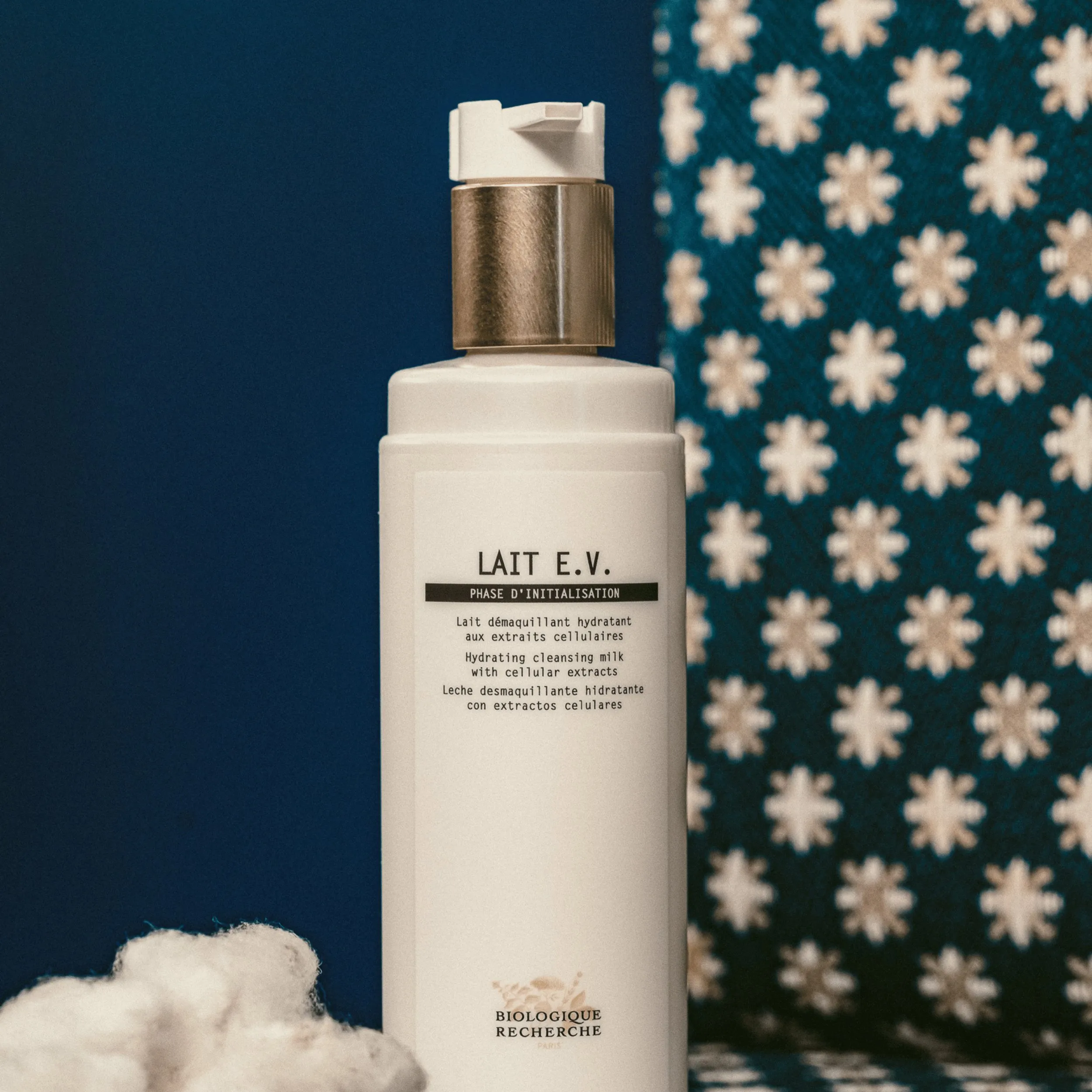Flacone bianco di latte detergente idratante Biologique Recherche Lait E.V. su sfondo floreale blu.