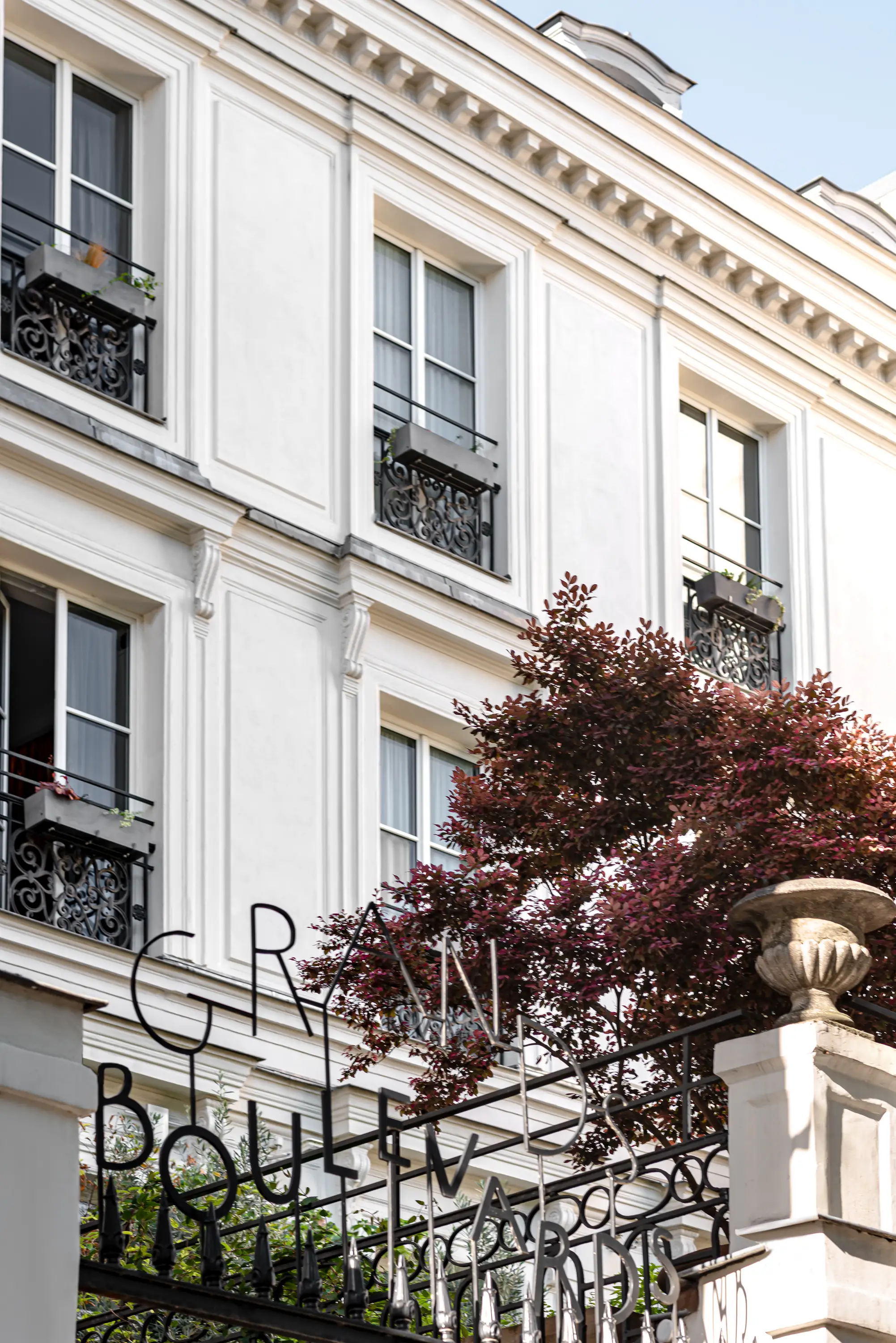 Fachada blanca del edificio con balcones de hierro forjado negro y un letrero que dice «Grands Boulevards».