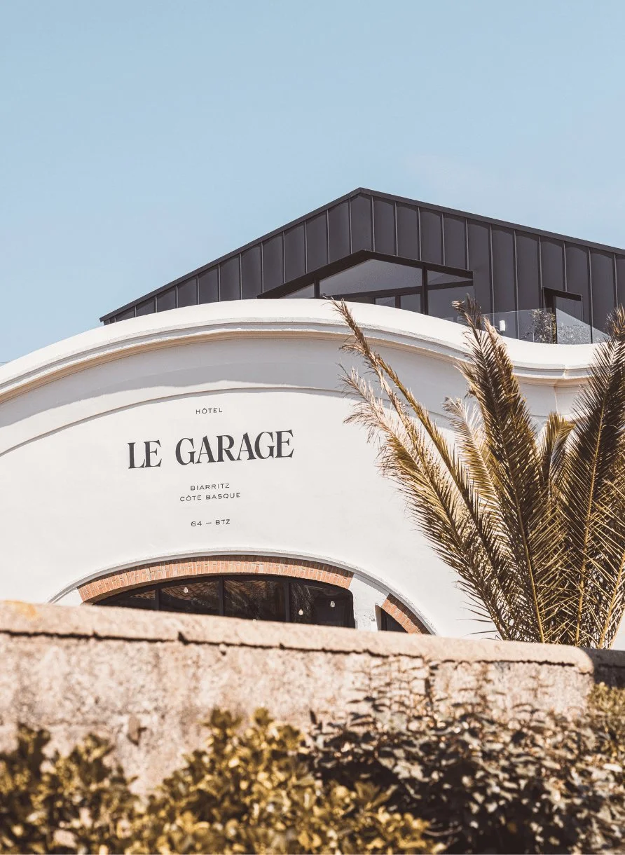 Esterno dell'Hôtel Le Garage a Biarritz con palme e moderna struttura sul tetto.