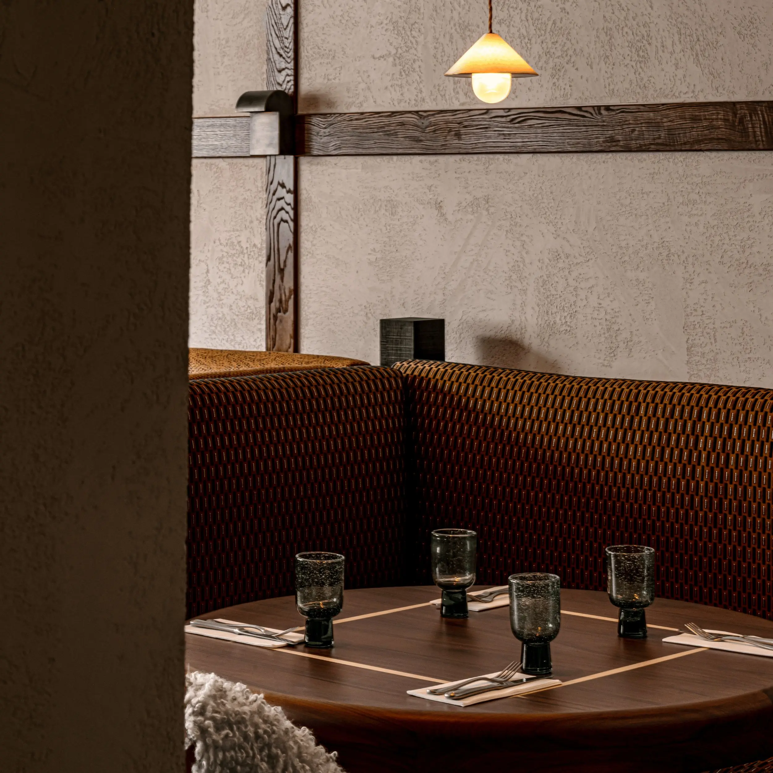 Restaurante aconchegante com uma mesa redonda de madeira com quatro copos escuros e talheres.