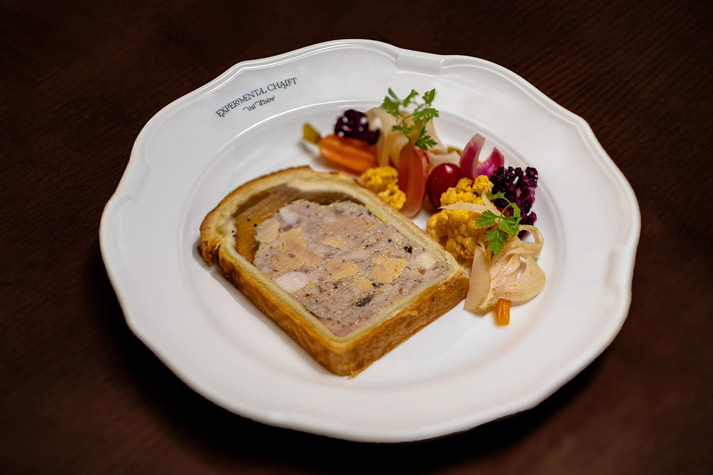 Fatia de terrina com vegetais em conserva misturados em um prato branco do Experimenta Chalet.
