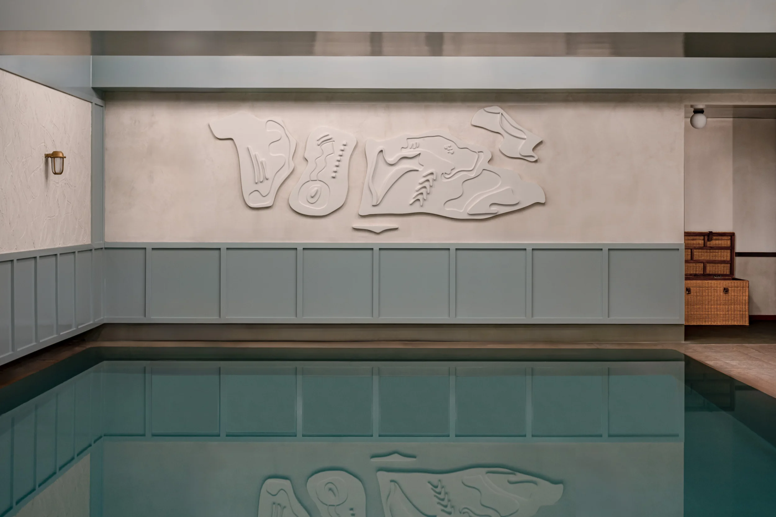 Indoor pool with calm water reflecting a wall with abstract white art and blue wainscoting.