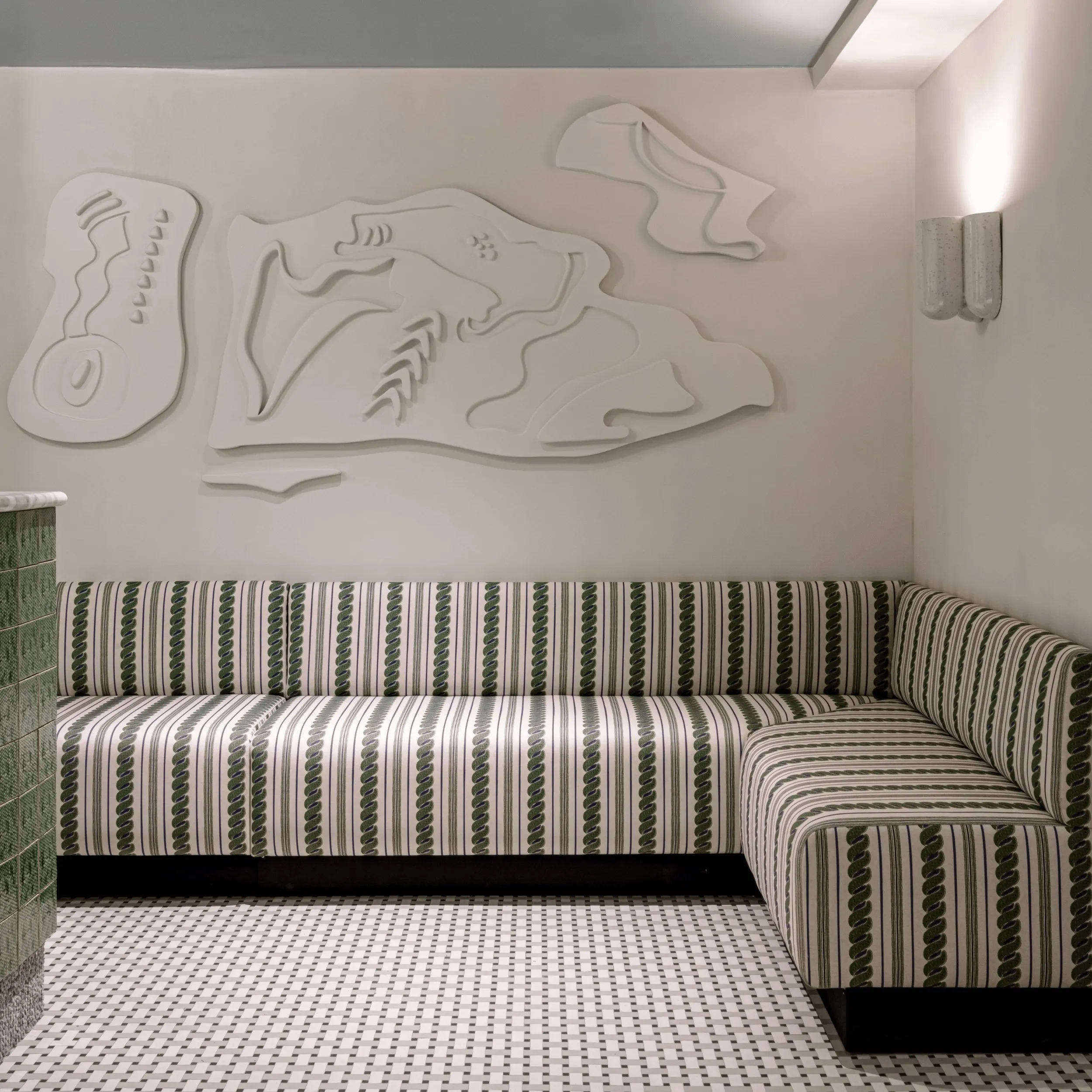 Sofá listrado em forma de L em verde e branco em uma sala minimalista com arte abstrata na parede acima dela.
