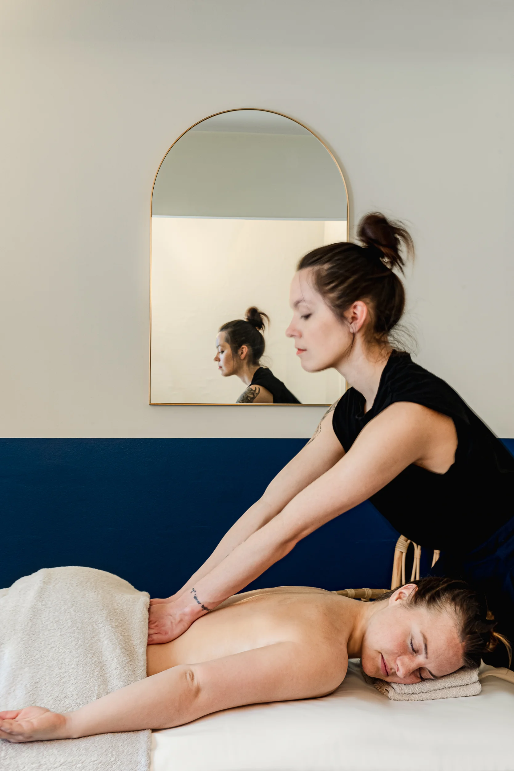 Terapista che fa un massaggio alla schiena a una donna sdraiata a faccia in giù su un lettino da spa con un asciugamano.
