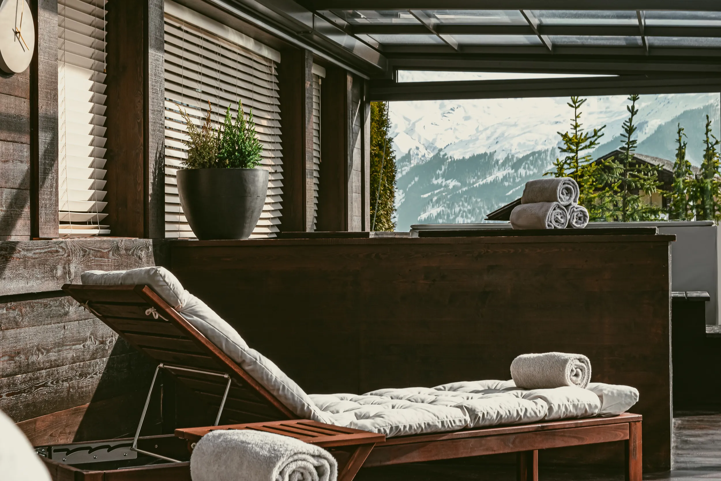 Poltrona in legno con cuscini e asciugamani arrotolati su un patio con vista sulle montagne coperte di neve.