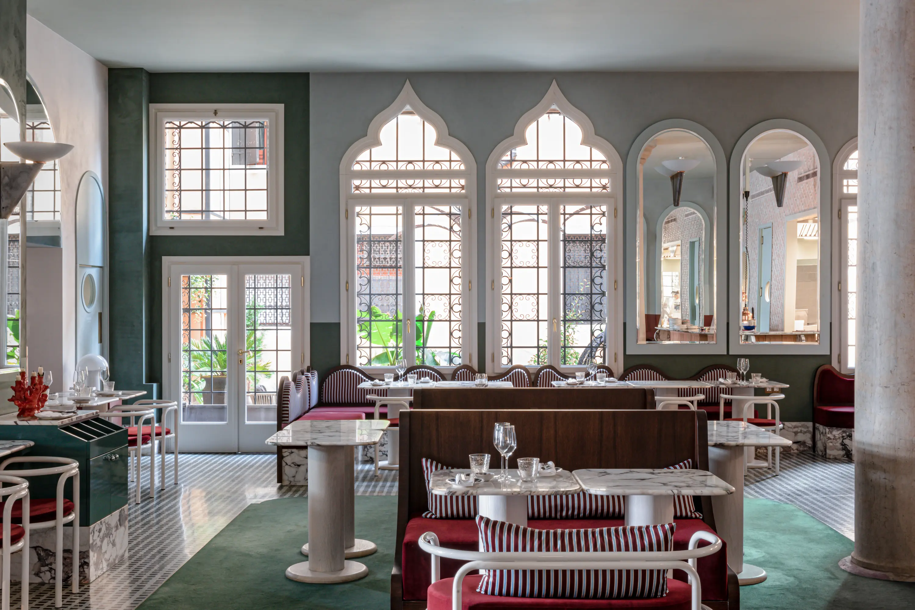 Elegant restaurant interior with marble tables, red cushioned seating, arched windows, and mirrors.