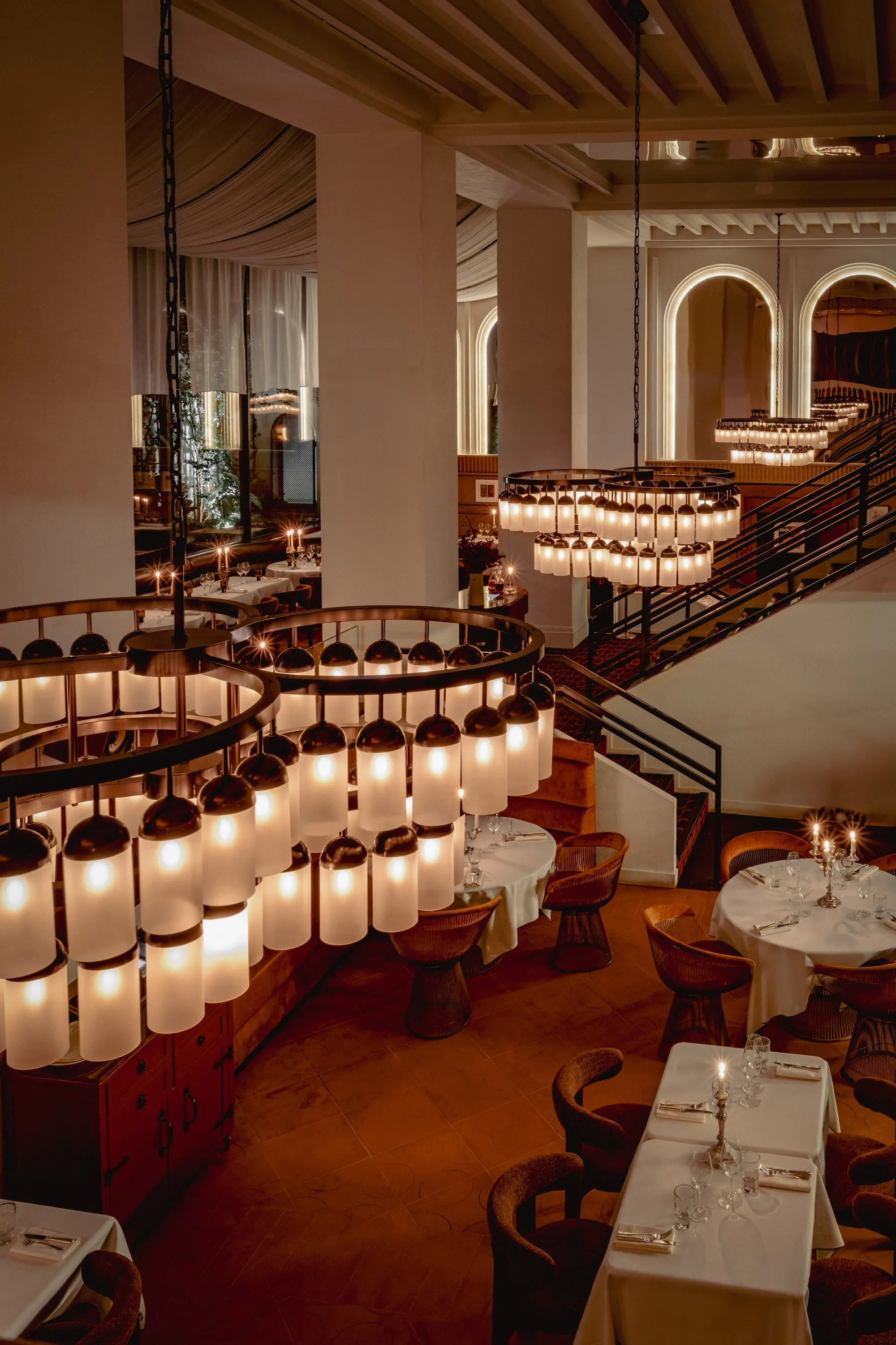 Elegant restaurant interior with round chandeliers, white tablecloths, and neatly arranged tables and chairs.