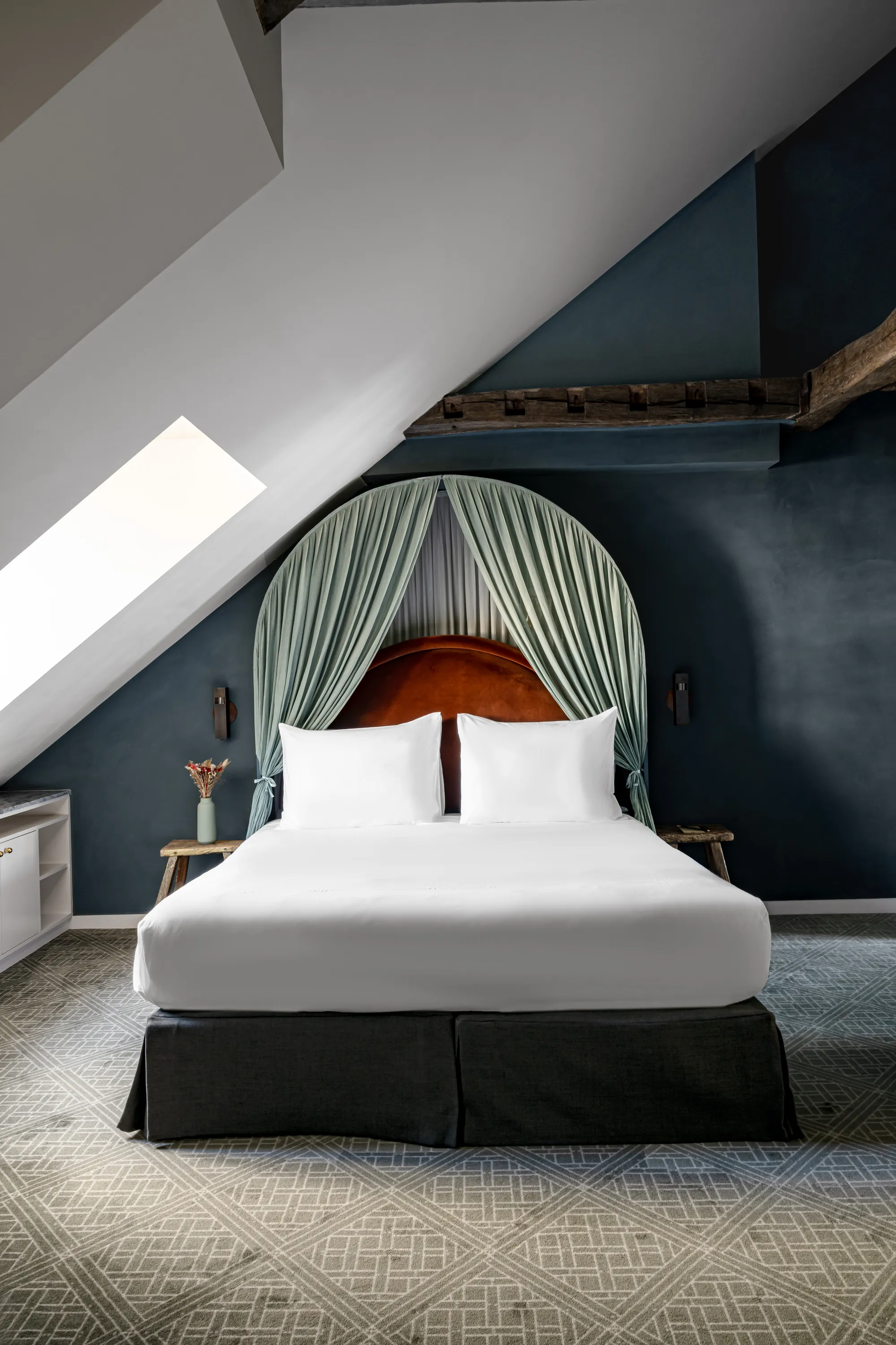 Modern bedroom with angled ceiling, gray walls, a bed with white linens, and a green canopy.