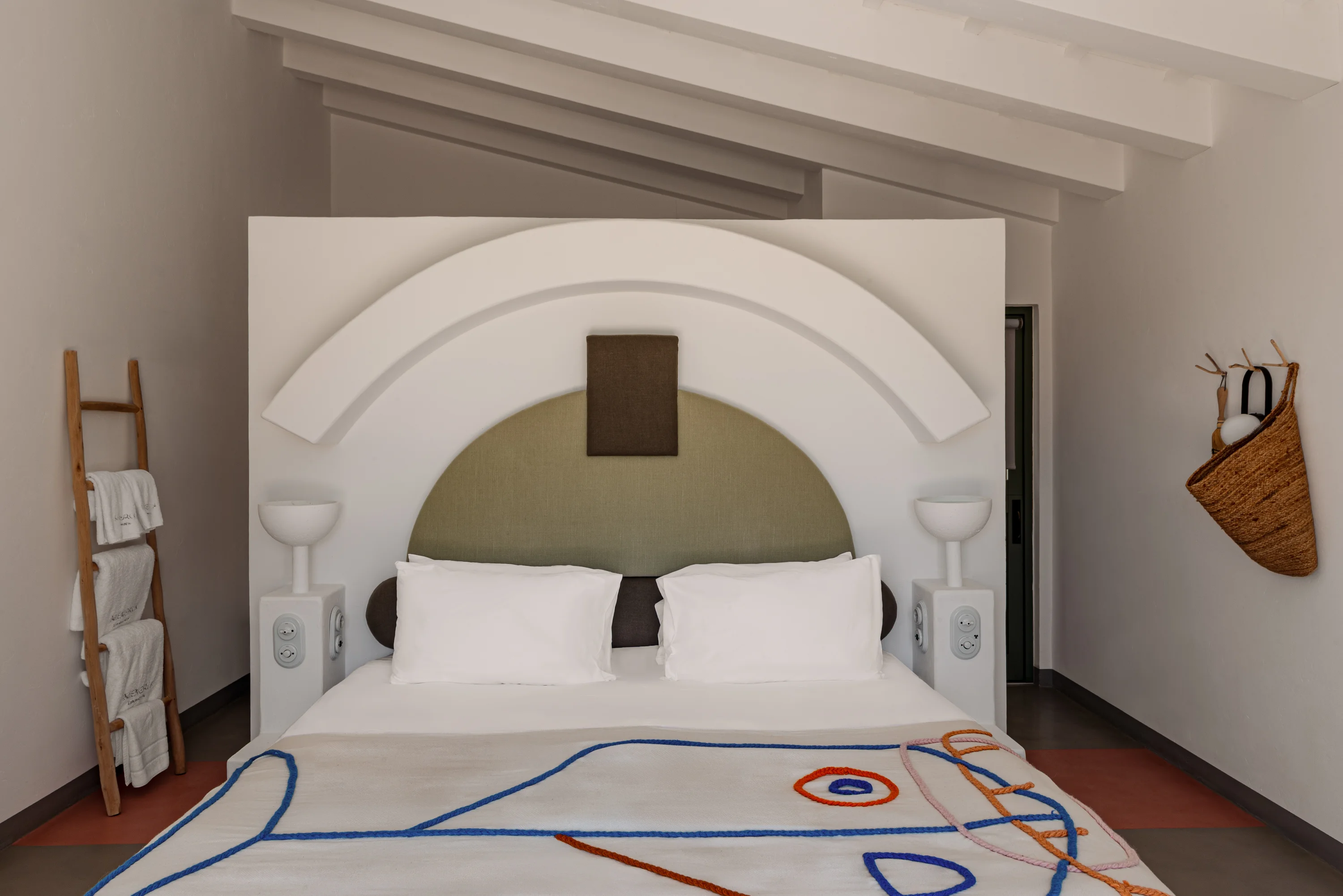 Minimalist bedroom with a decorative arch headboard, white pillows, and abstract pattern blanket.