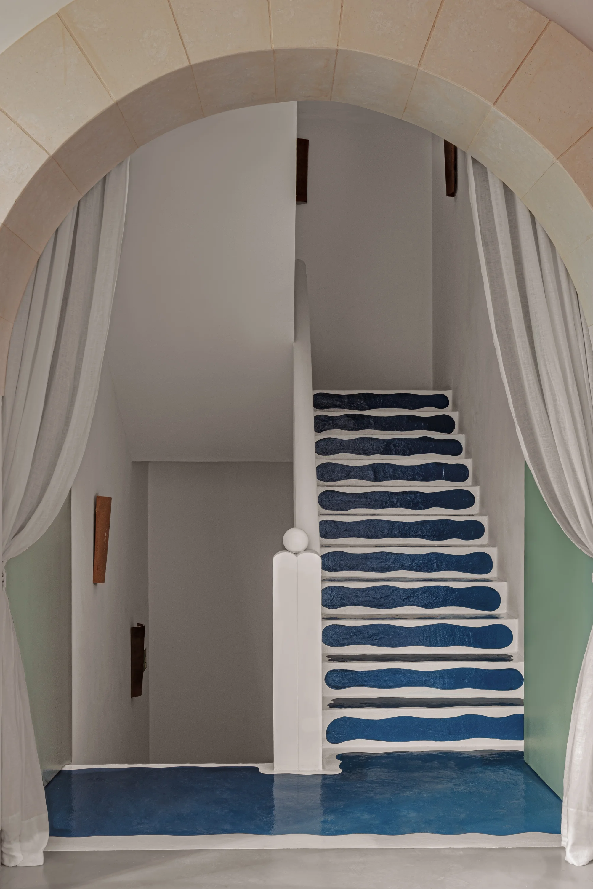 White staircase with blue irregular stripes and archway framed by white curtains.