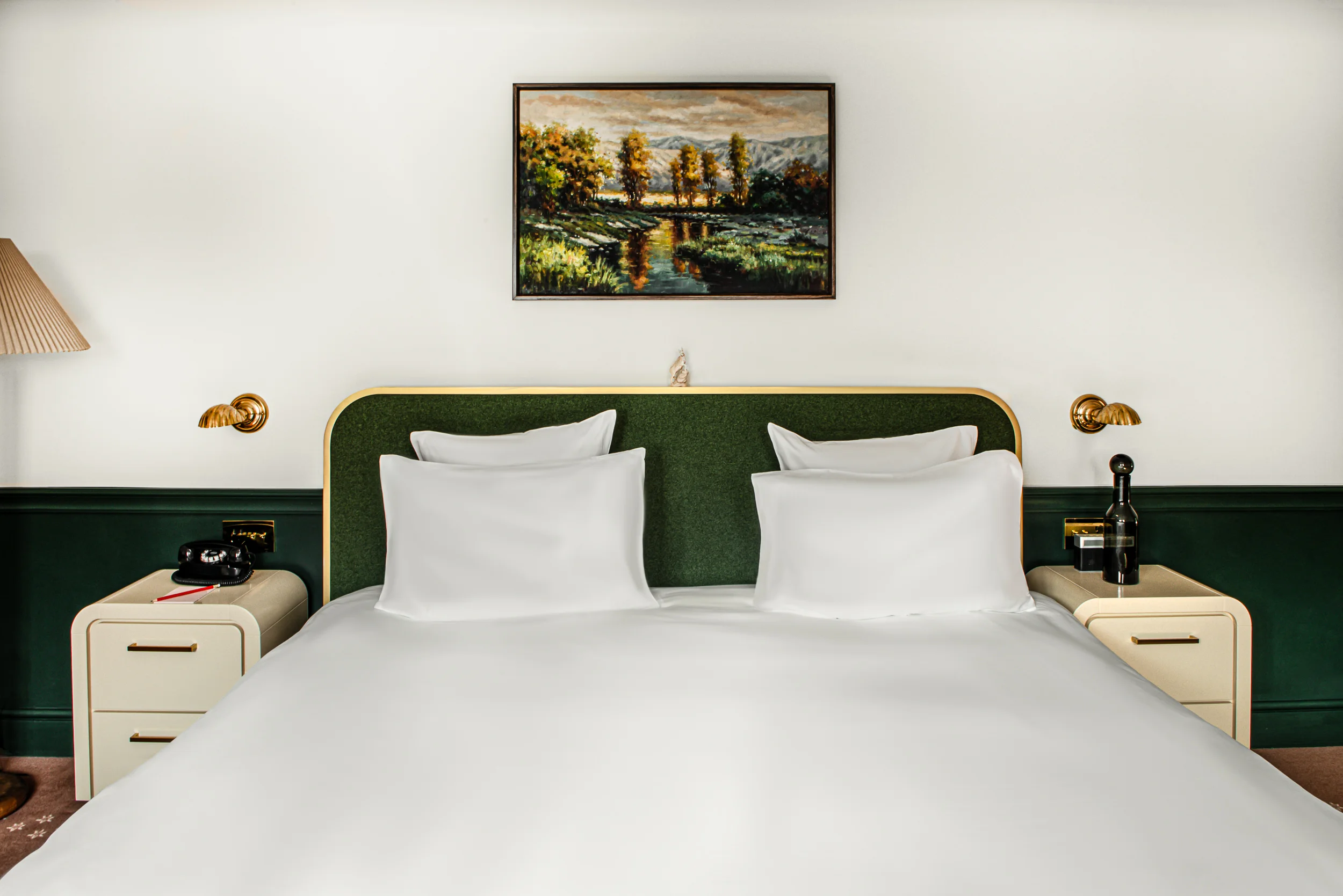 Modern bed with green headboard, white pillows and bedding, nightstands, lamps, and landscape painting