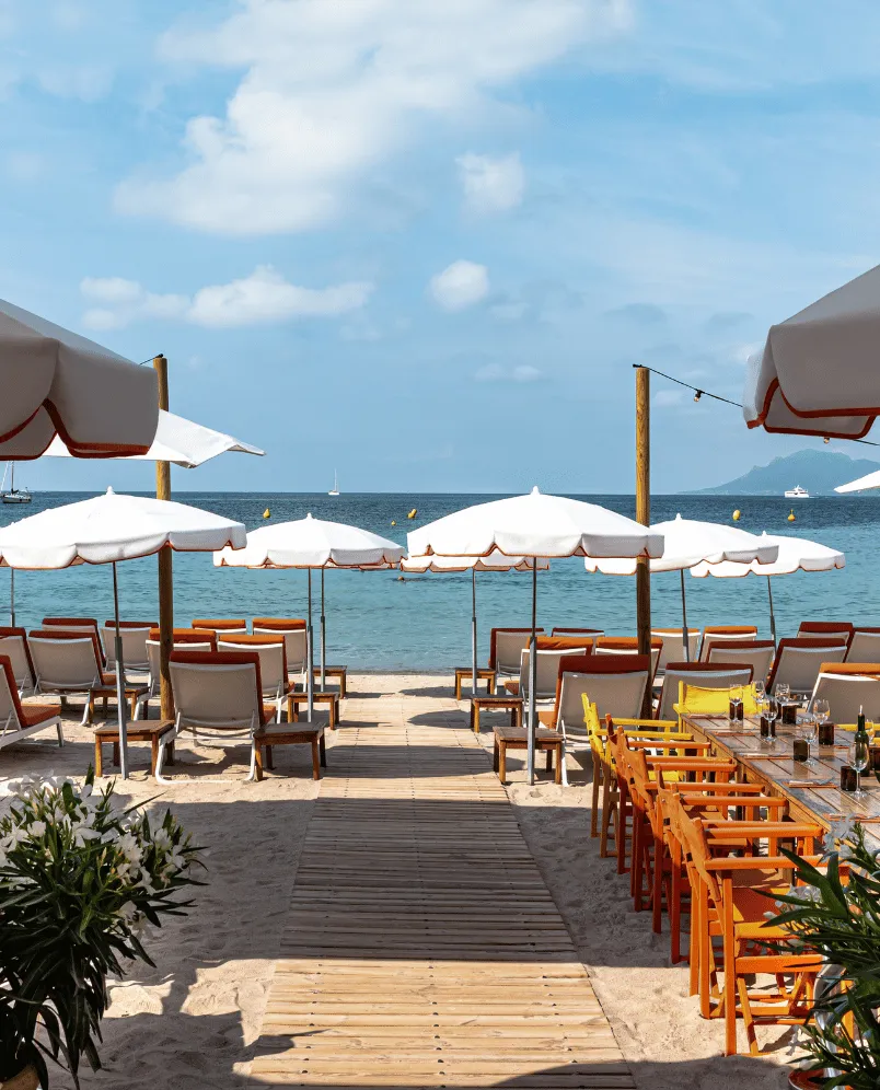 Frente a la playa con sombrillas blancas, tumbonas y un comedor al aire libre junto al mar.