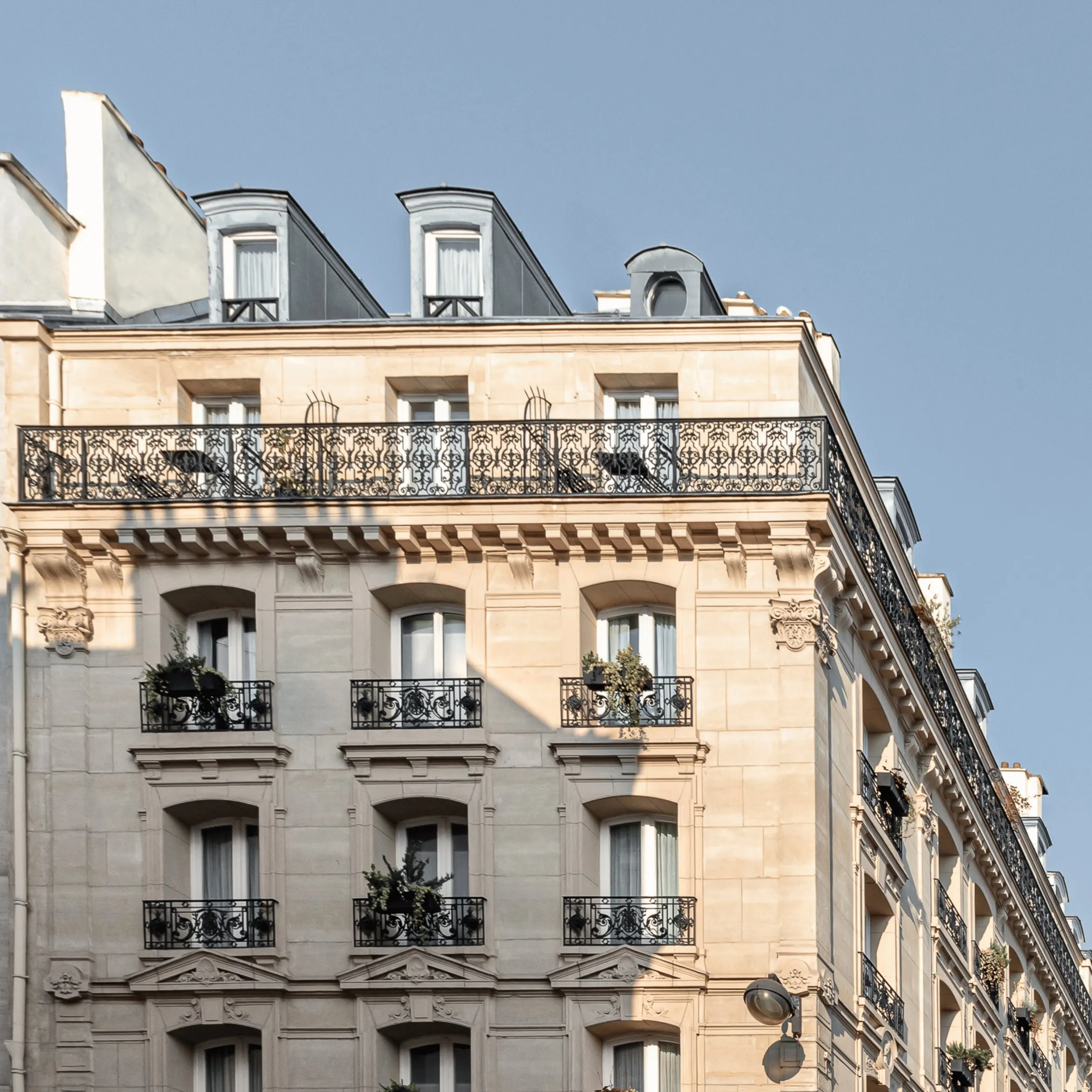 Parisian beige stone building with black wrought-iron balconies and plants under a clear sky.