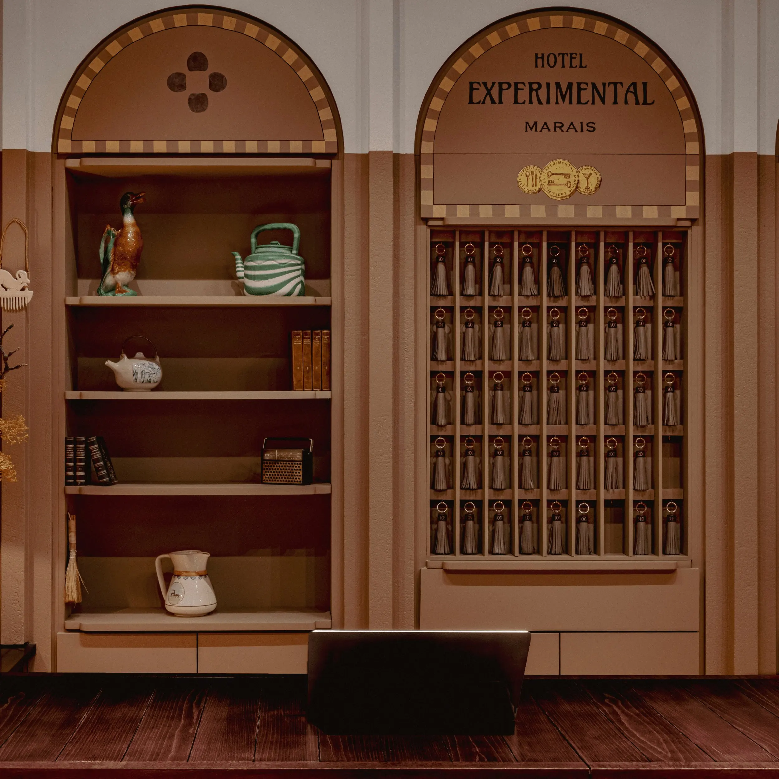 Hotel Experimental Marais reception with wooden desk, shelves, and multiple key holders with tassels.
