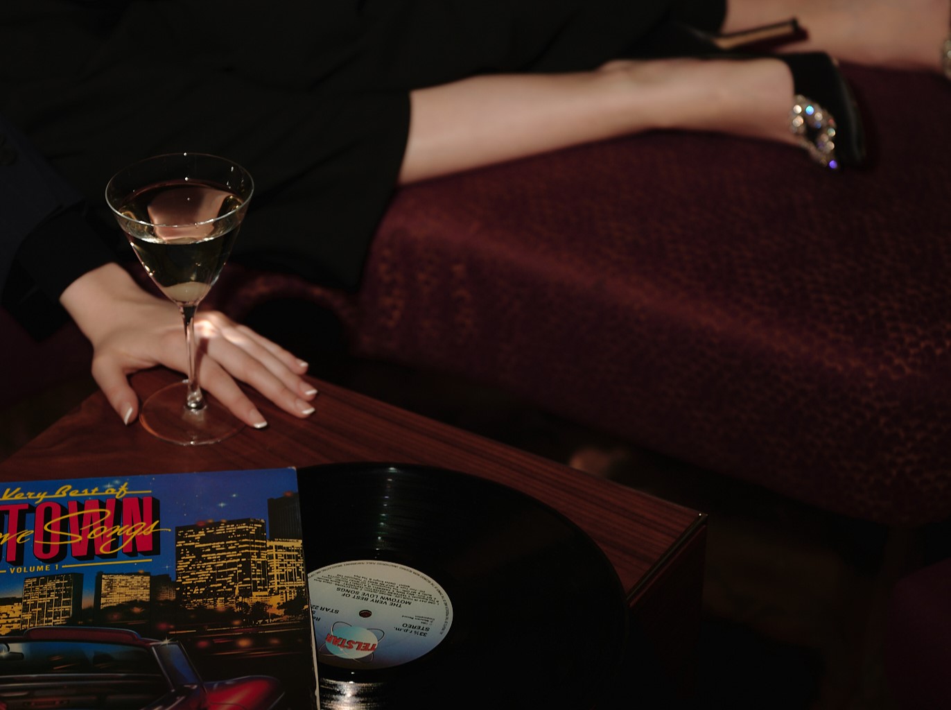 Hand resting on a table near a wine glass and a vinyl record with a cityscape album cover.