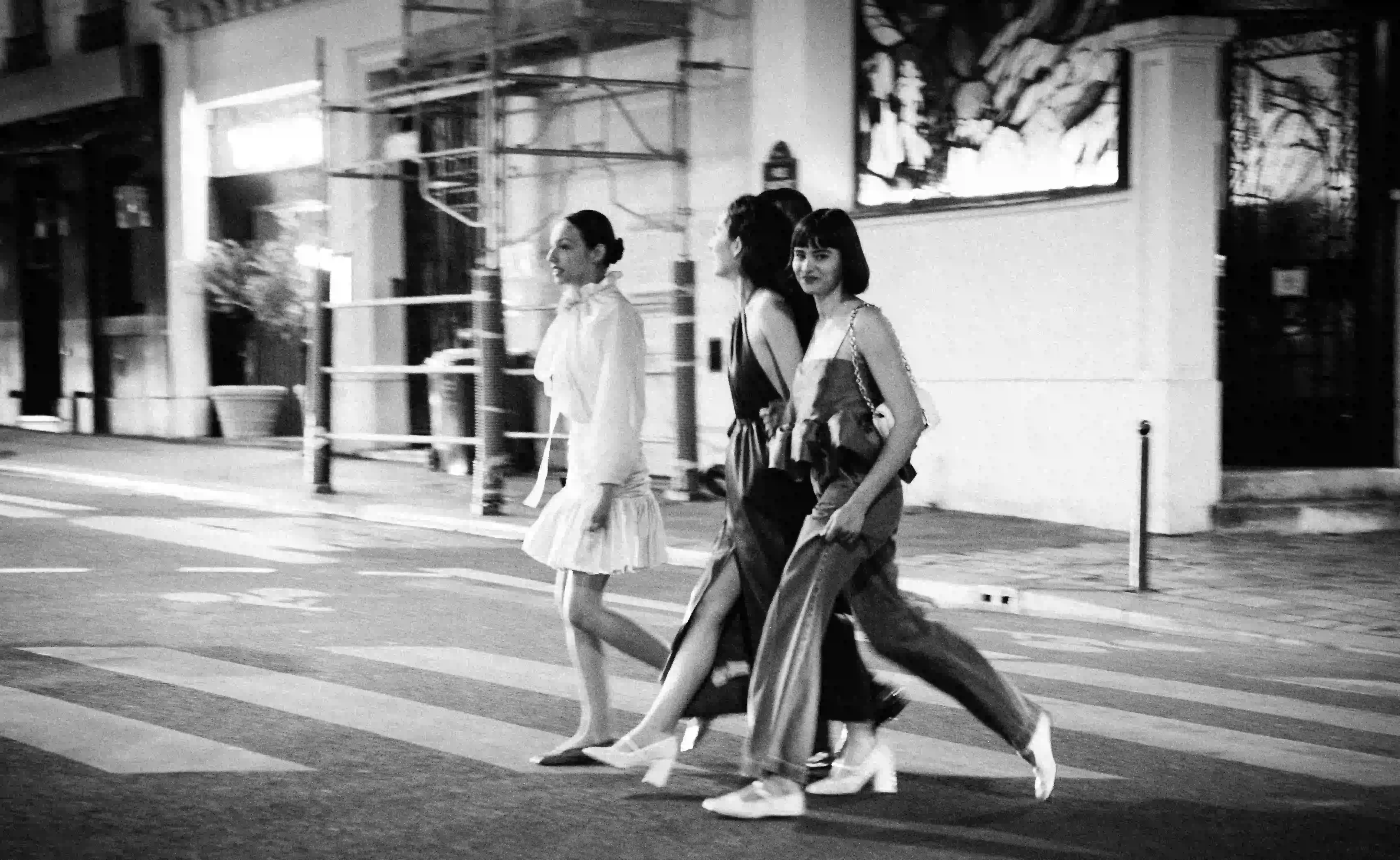 Cuatro mujeres vestidas con estilo paseando juntas por un paso peatonal de la ciudad por la noche vestidas de blanco y negro.