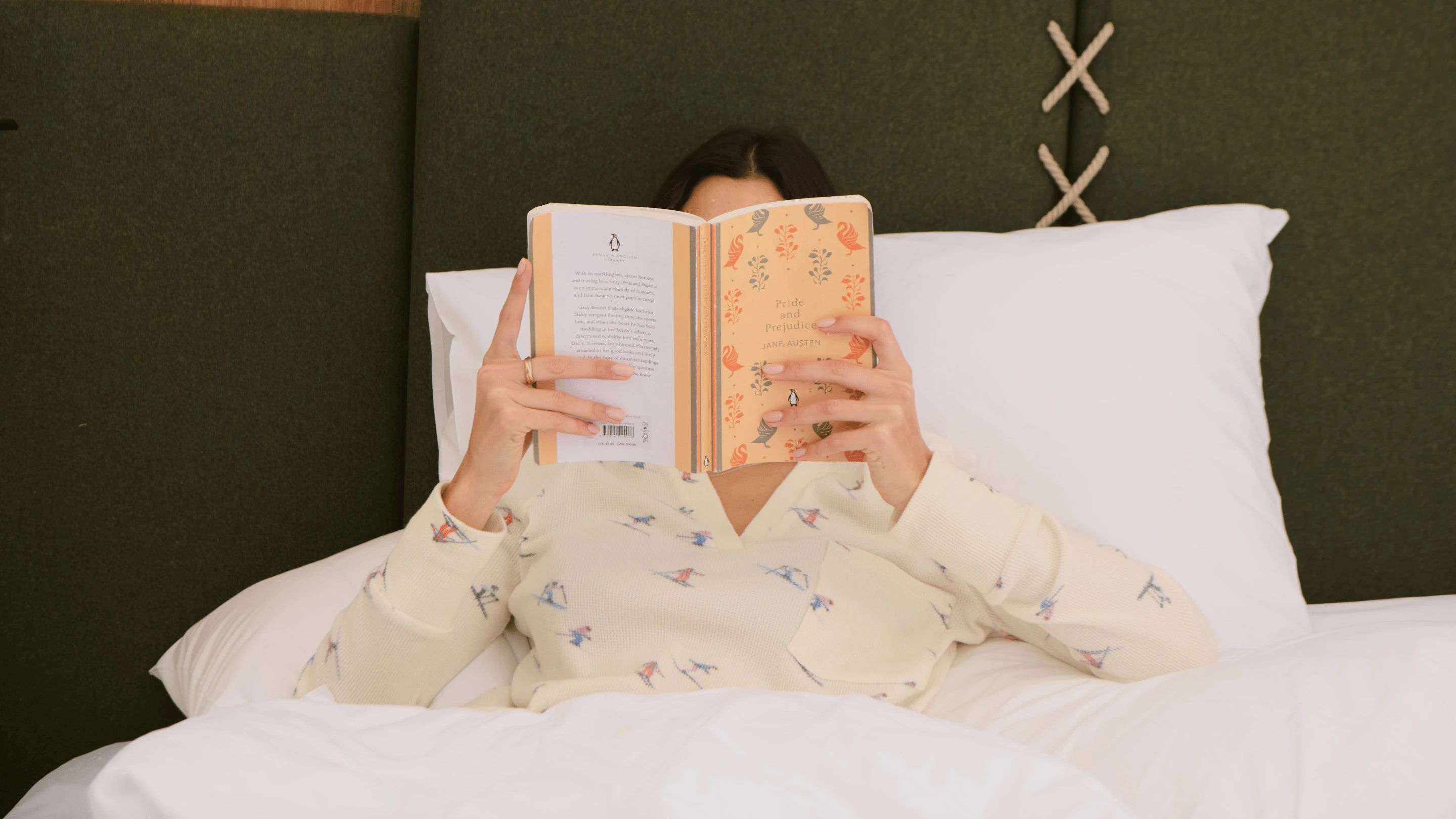 Pessoa deitada na cama lendo o livro Orgulho e Preconceito de Jane Austen.