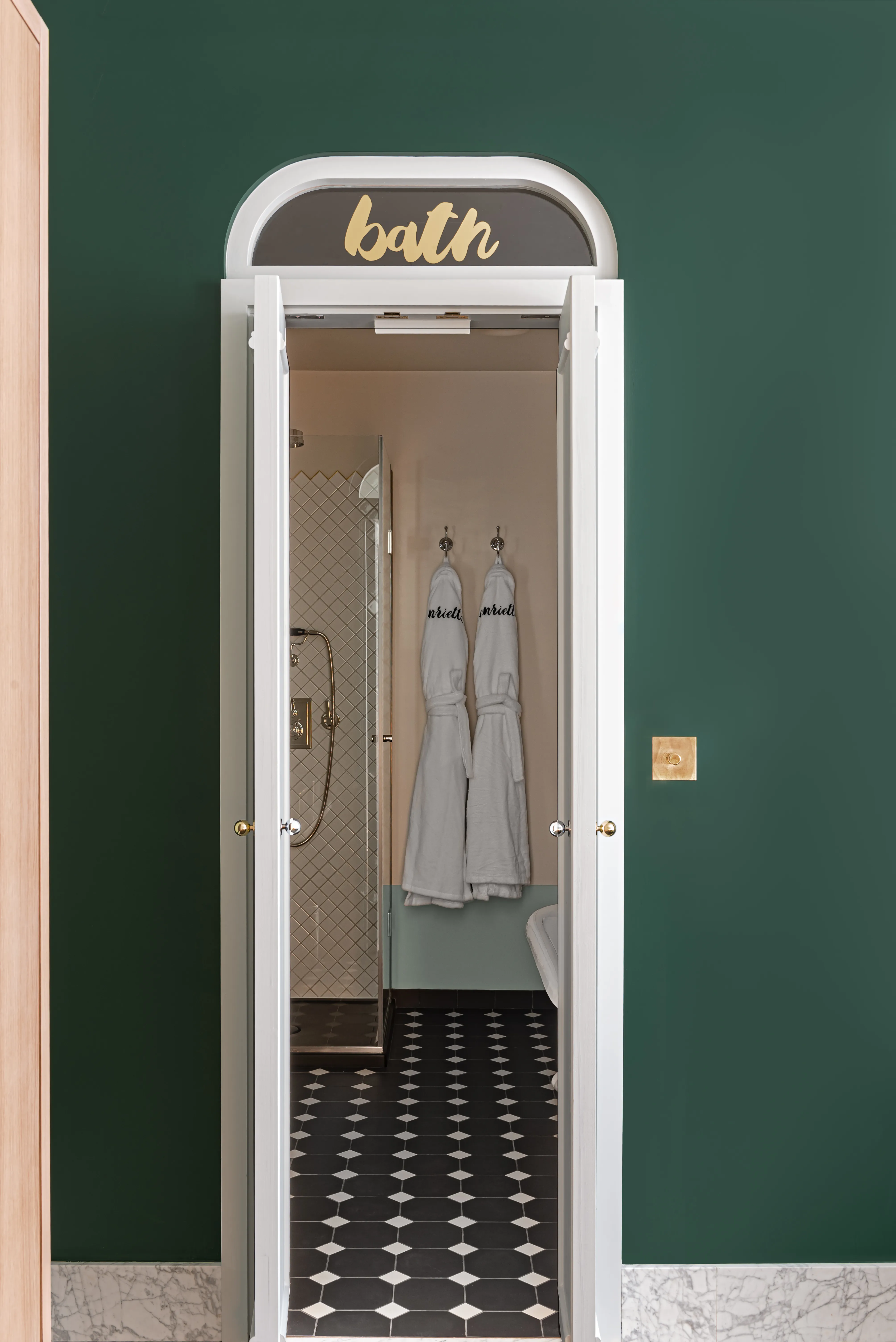 Open white door labeled 'bath' reveals bathroom with patterned floor, two hanging white robes, and tiled shower.