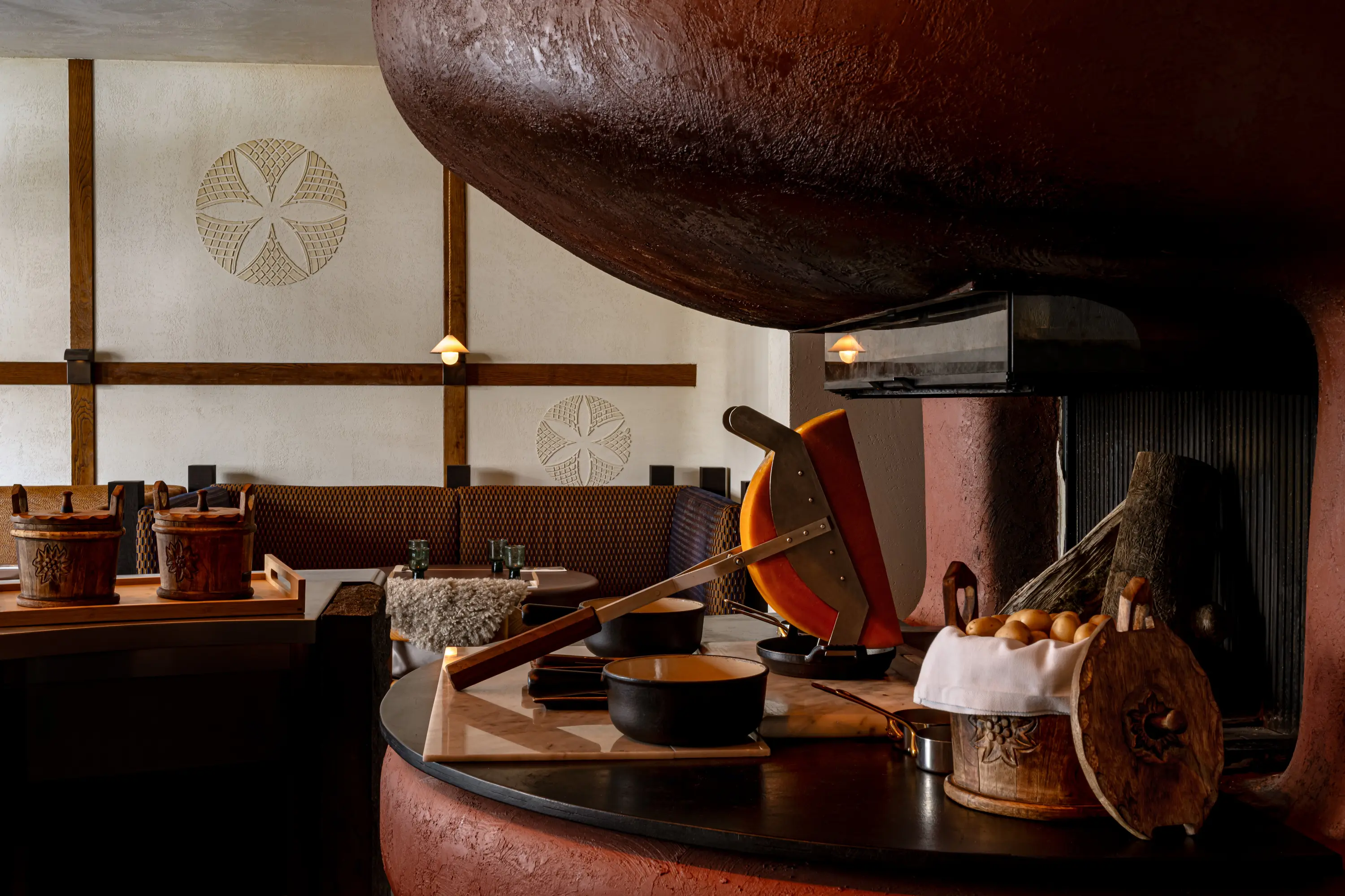 Cozy room with a raclette cheese melter, pots, basket of potatoes, and rustic decor near a fireplace.