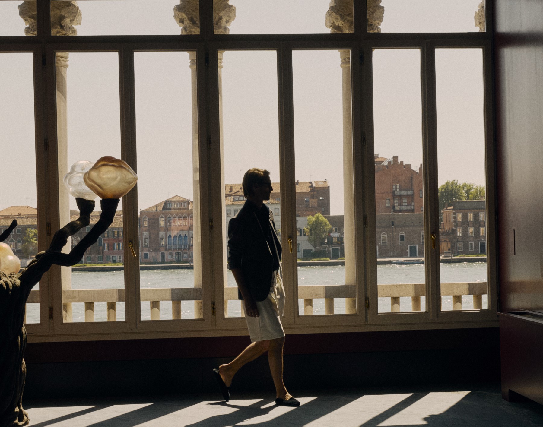 Silhouette di un uomo che cammina all'interno vicino a grandi finestre con vista sull'acqua e sugli edifici storici.