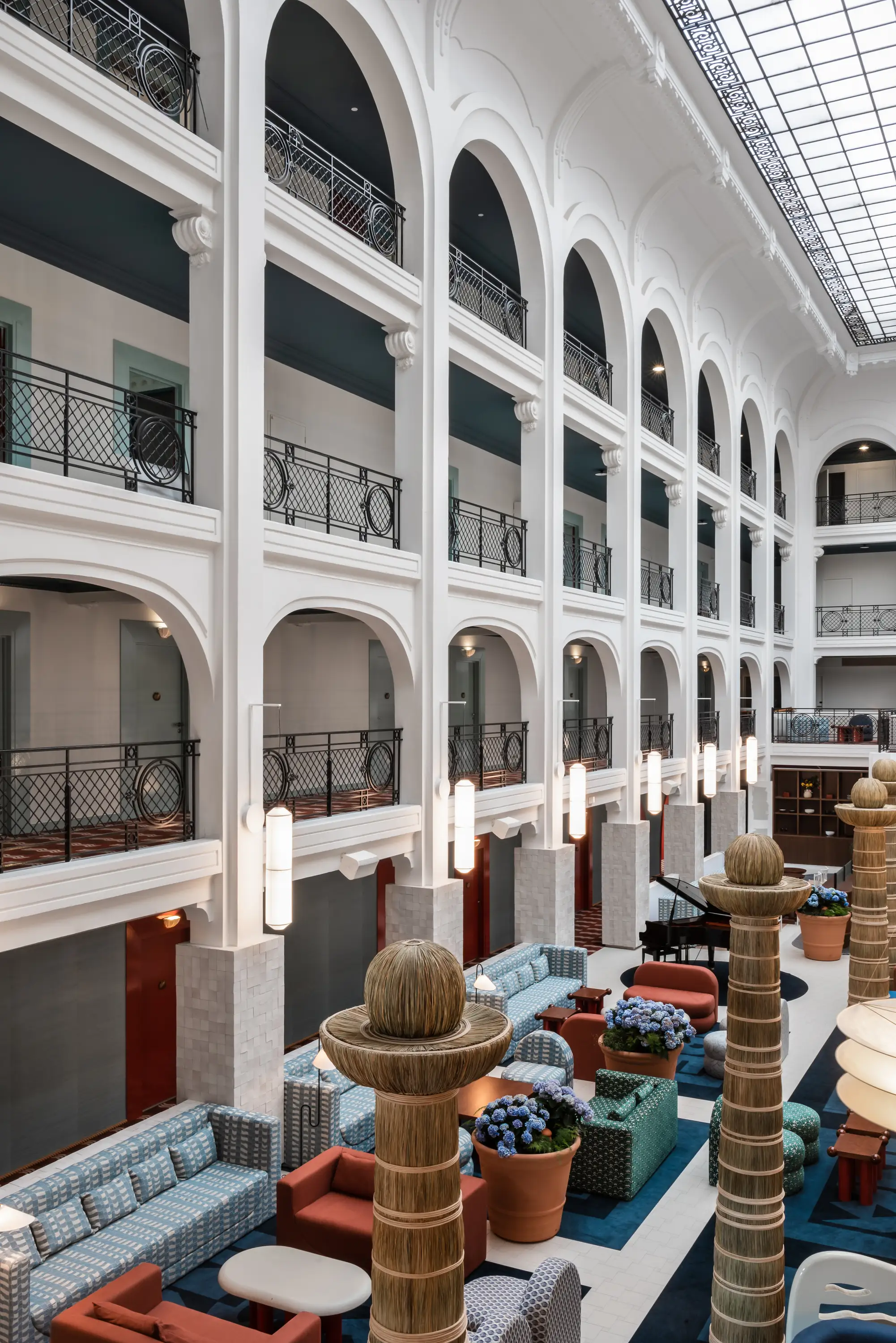 Hotel lobby with tall white arches, patterned seating, decorative columns, and a skylight ceiling.