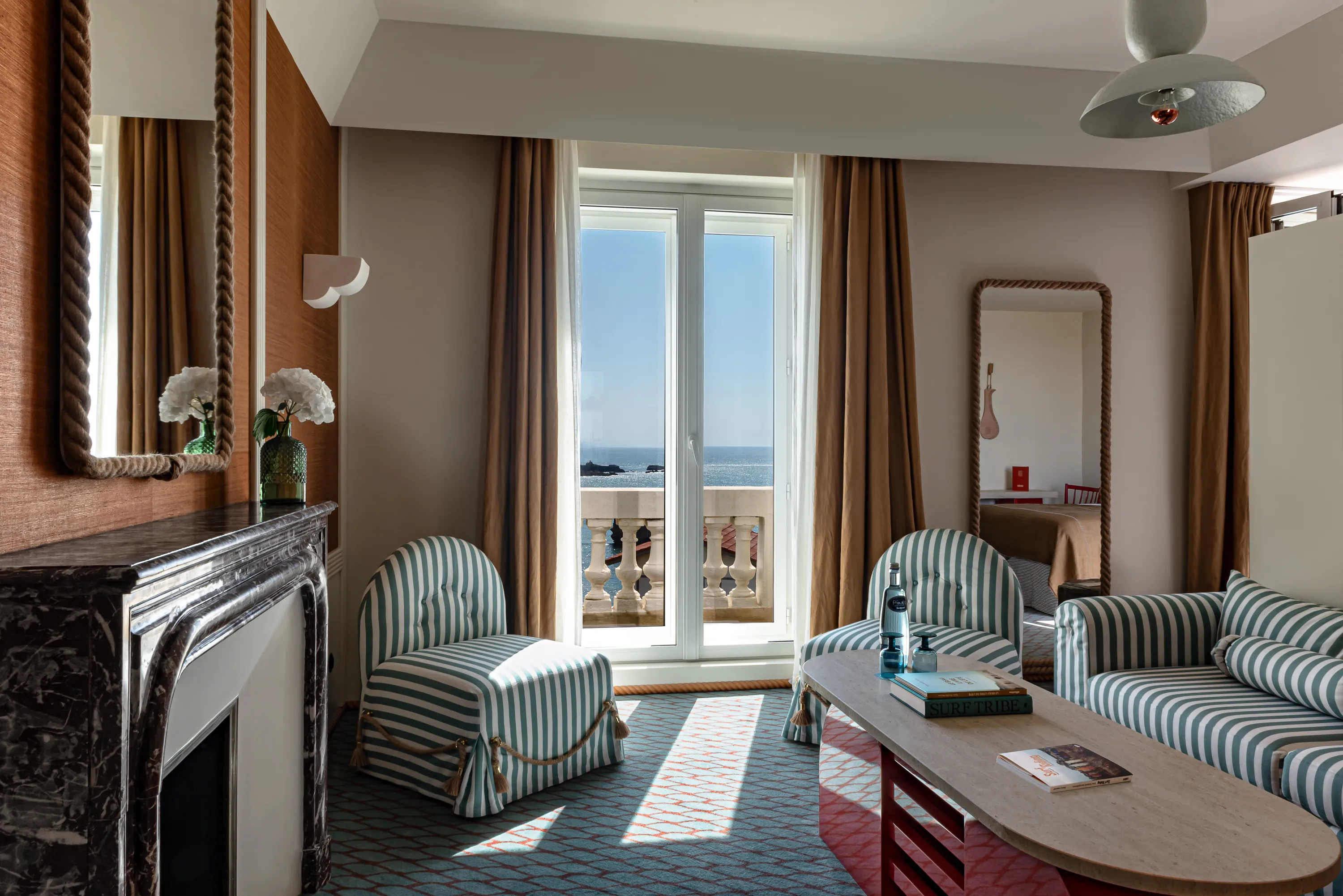 Hotel room with striped chairs, sofa, coffee table, fireplace, and balcony view of the ocean.