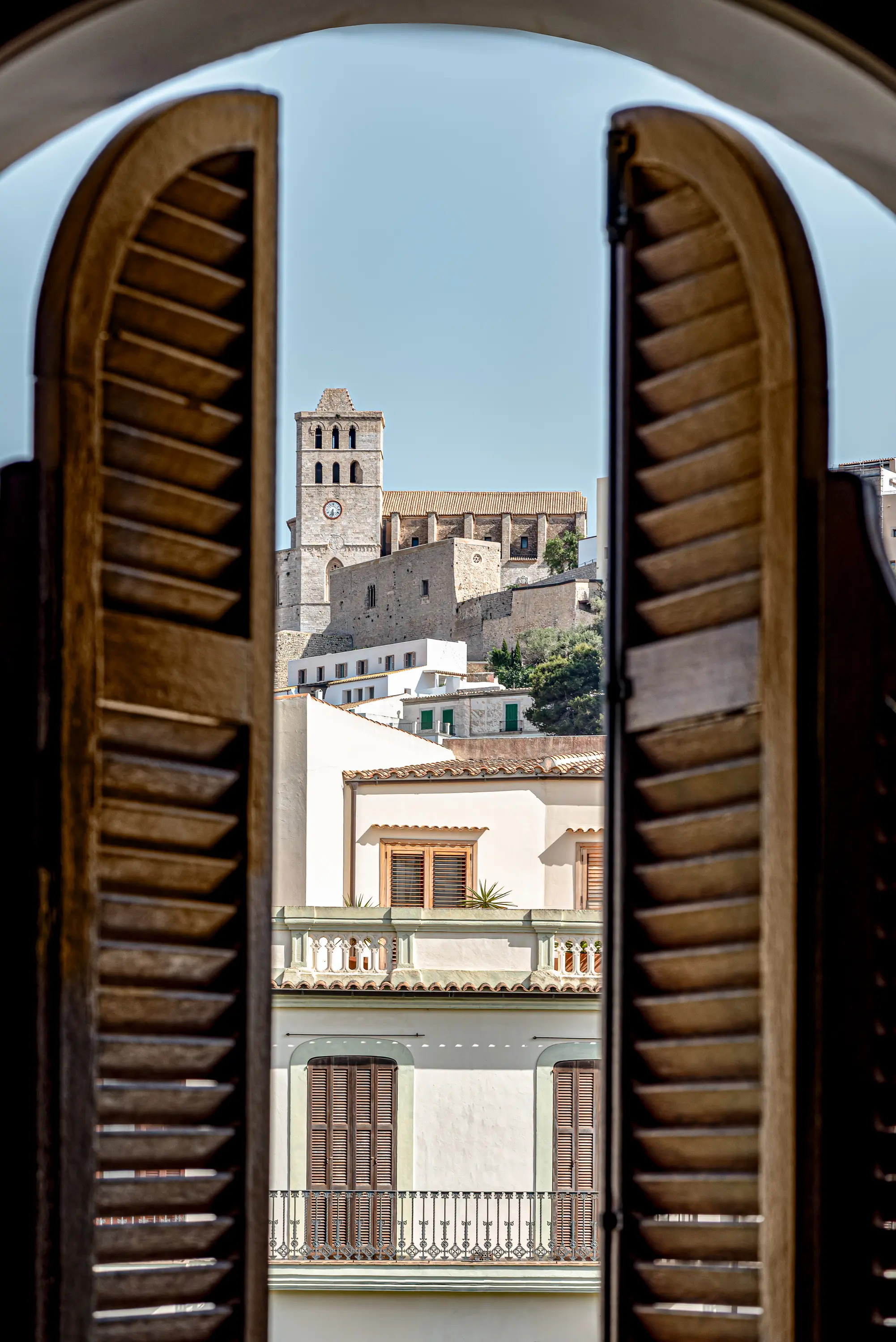 View of historic stone church tower and buildings through open wooden window shutters.