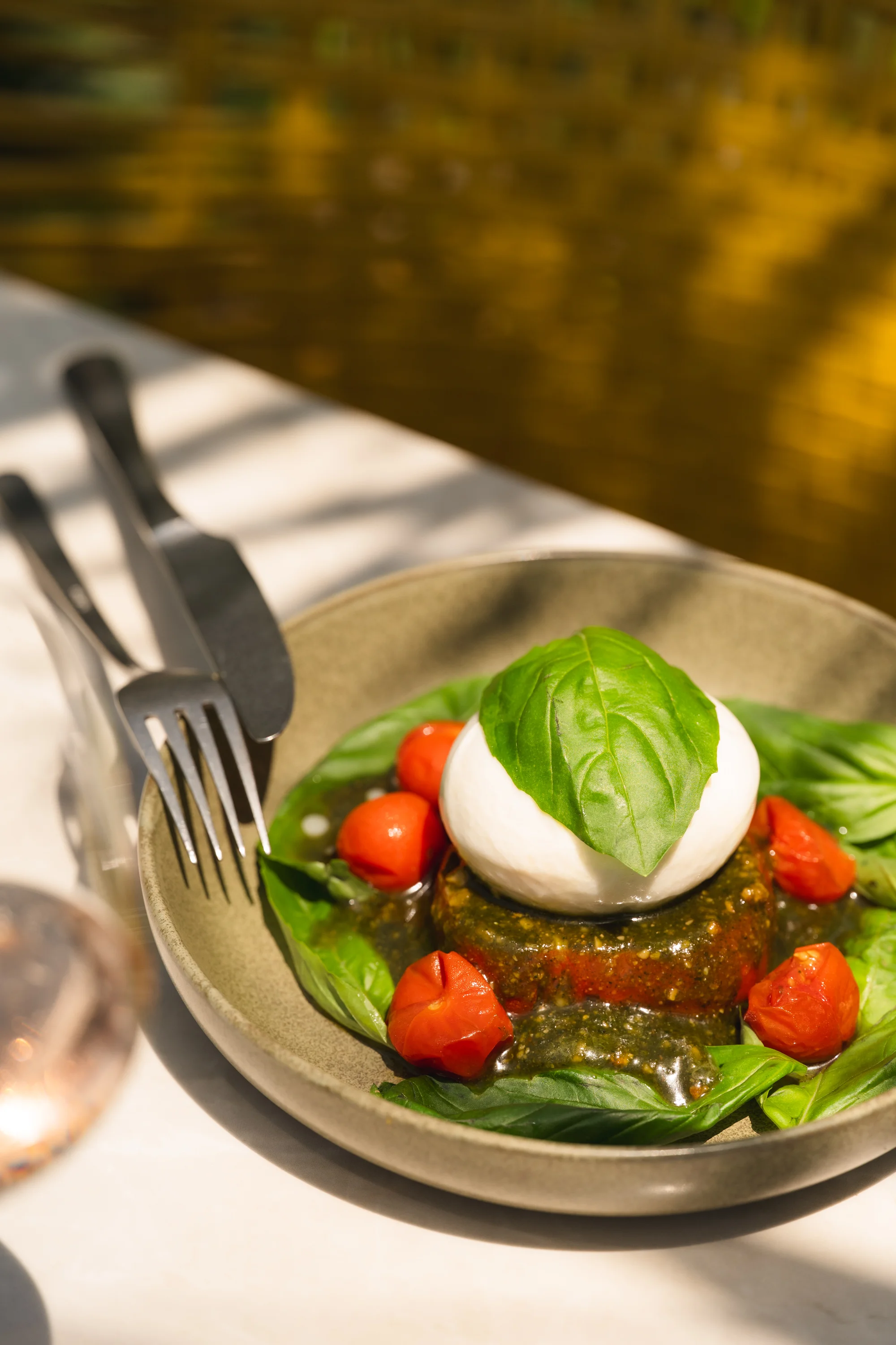 Plate with fresh mozzarella, basil leaf, cherry tomatoes, and pesto sauce on a white table.