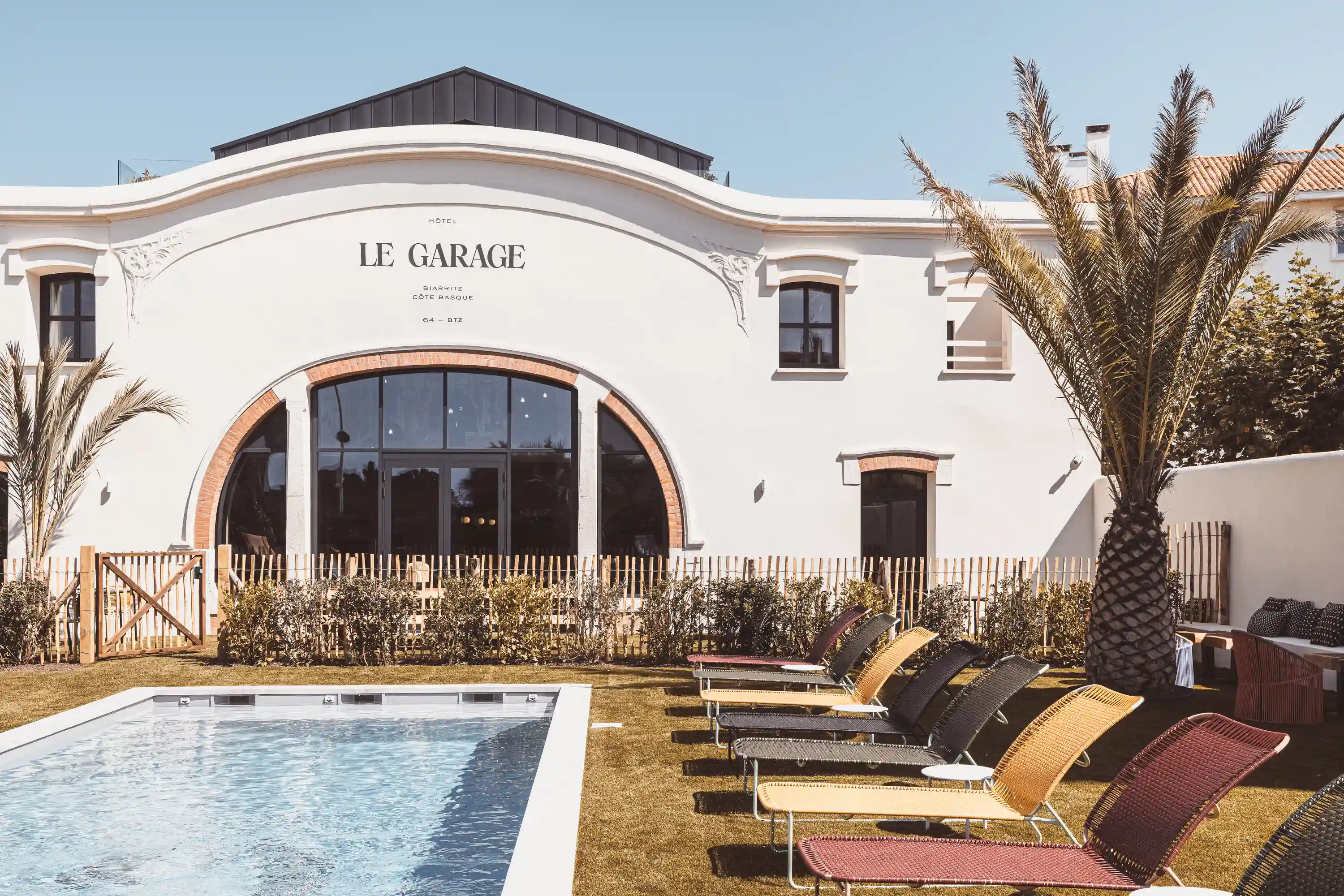 Outdoor pool with lounge chairs and palm trees in front of Hotel Le Garage building.