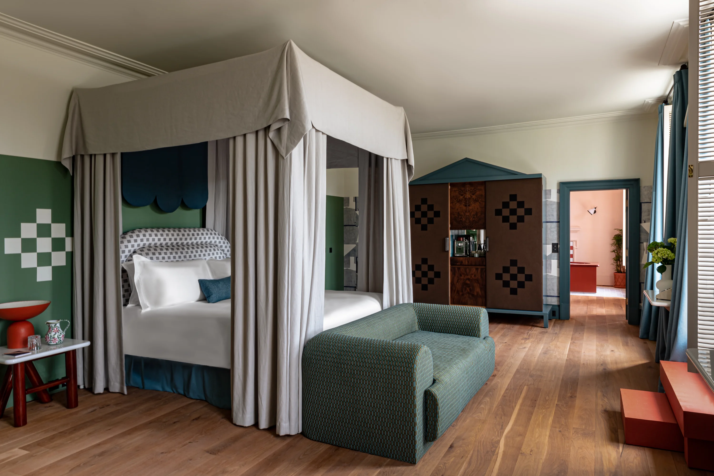 Hotel room with a canopy bed, green sofa, patterned wardrobe, and wooden flooring.