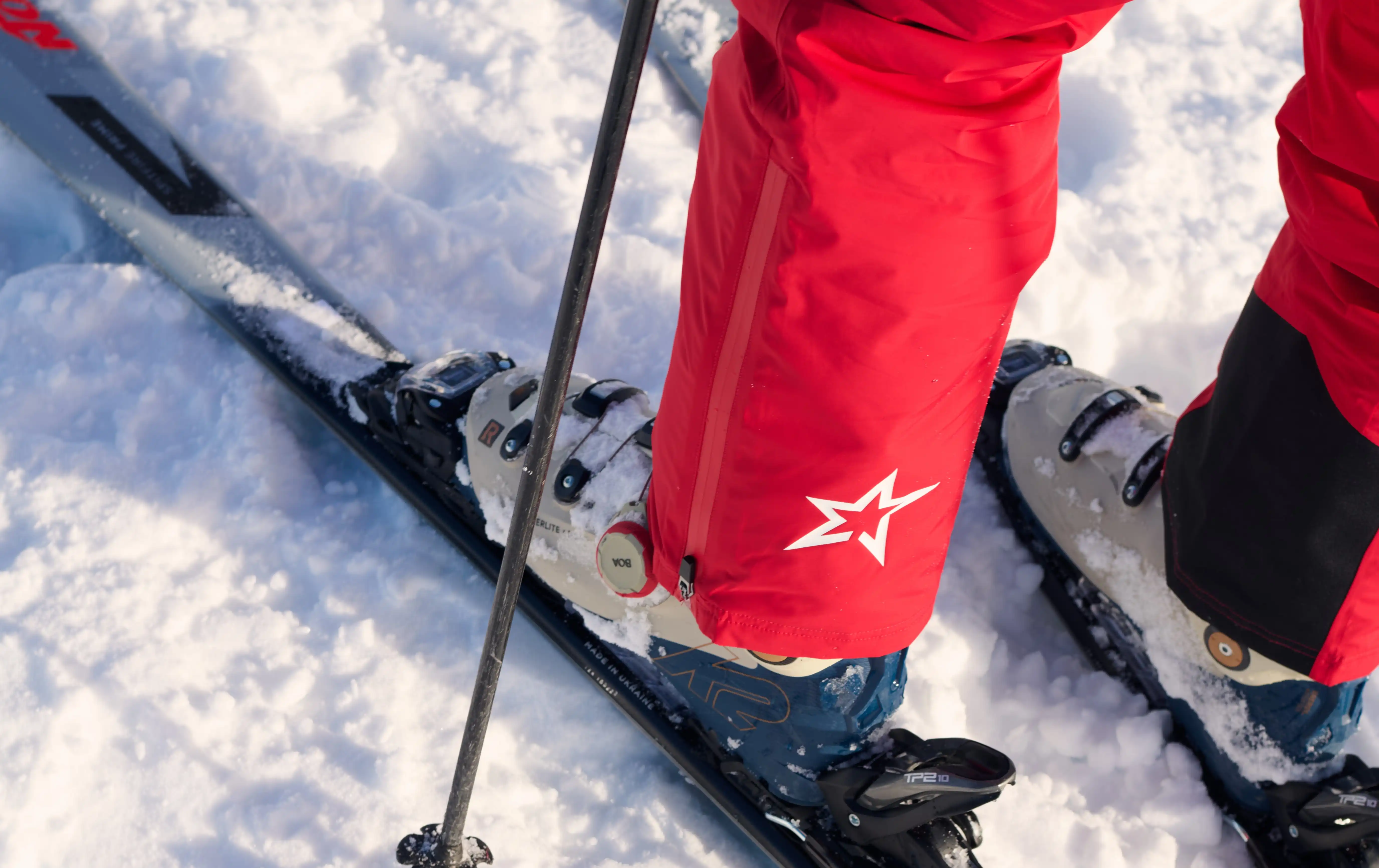 Close-up of skier's red pants and boots secured in black skis on snowy ground.