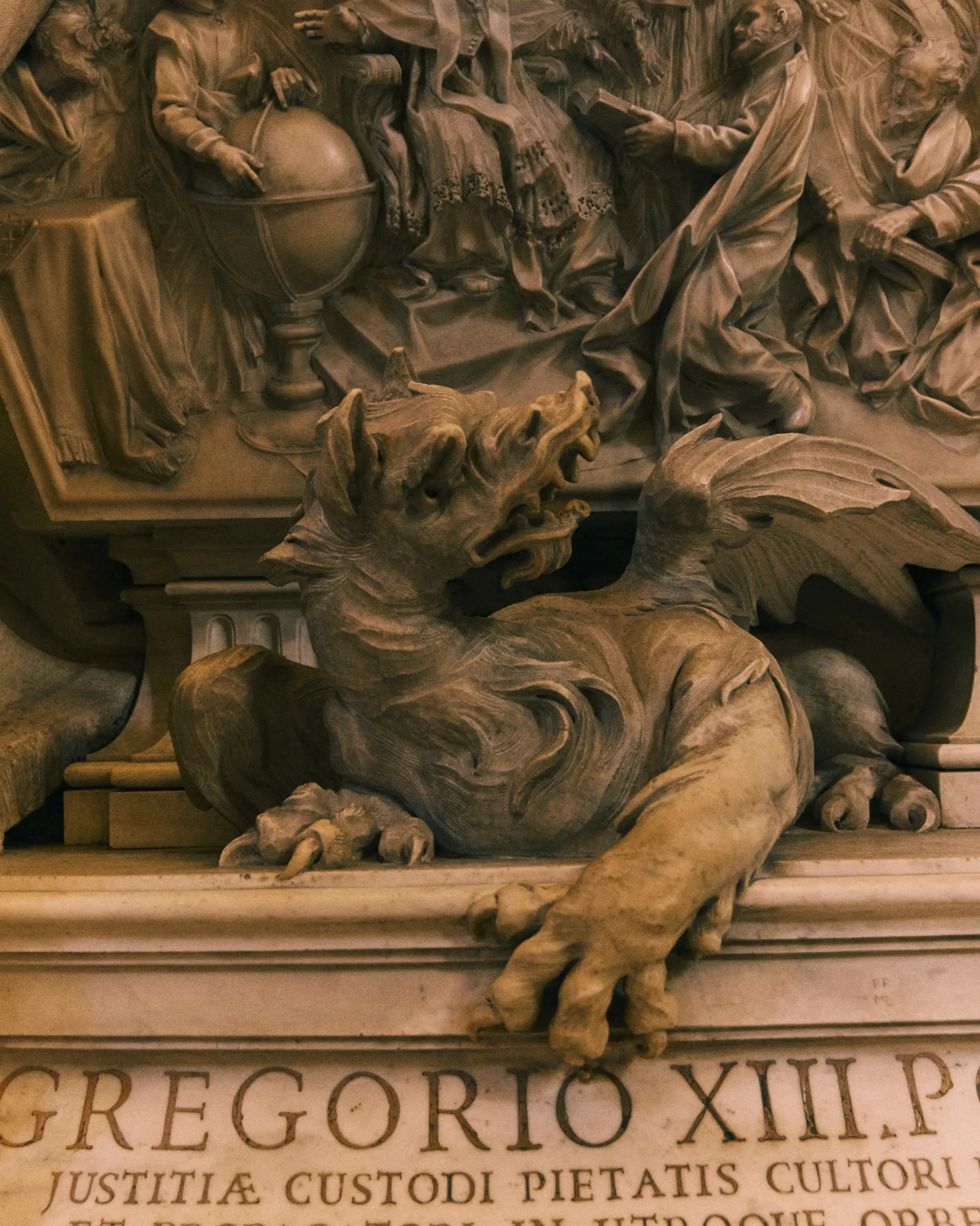 Stone sculpture of a dragon or winged creature beneath a detailed frieze of robed figures.