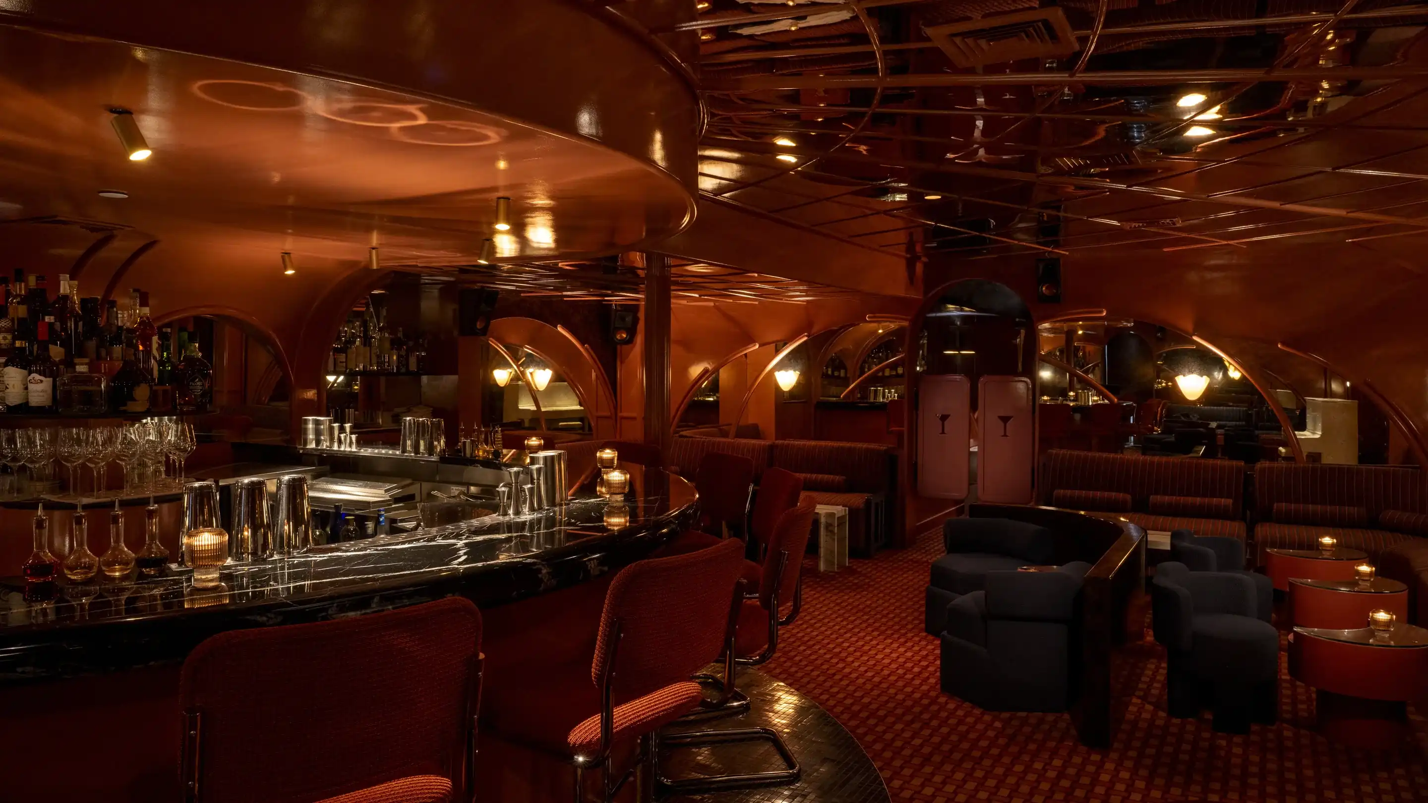 Bar vintage mal iluminado com balcão de mármore, assentos vermelhos e áreas de estar aconchegantes.