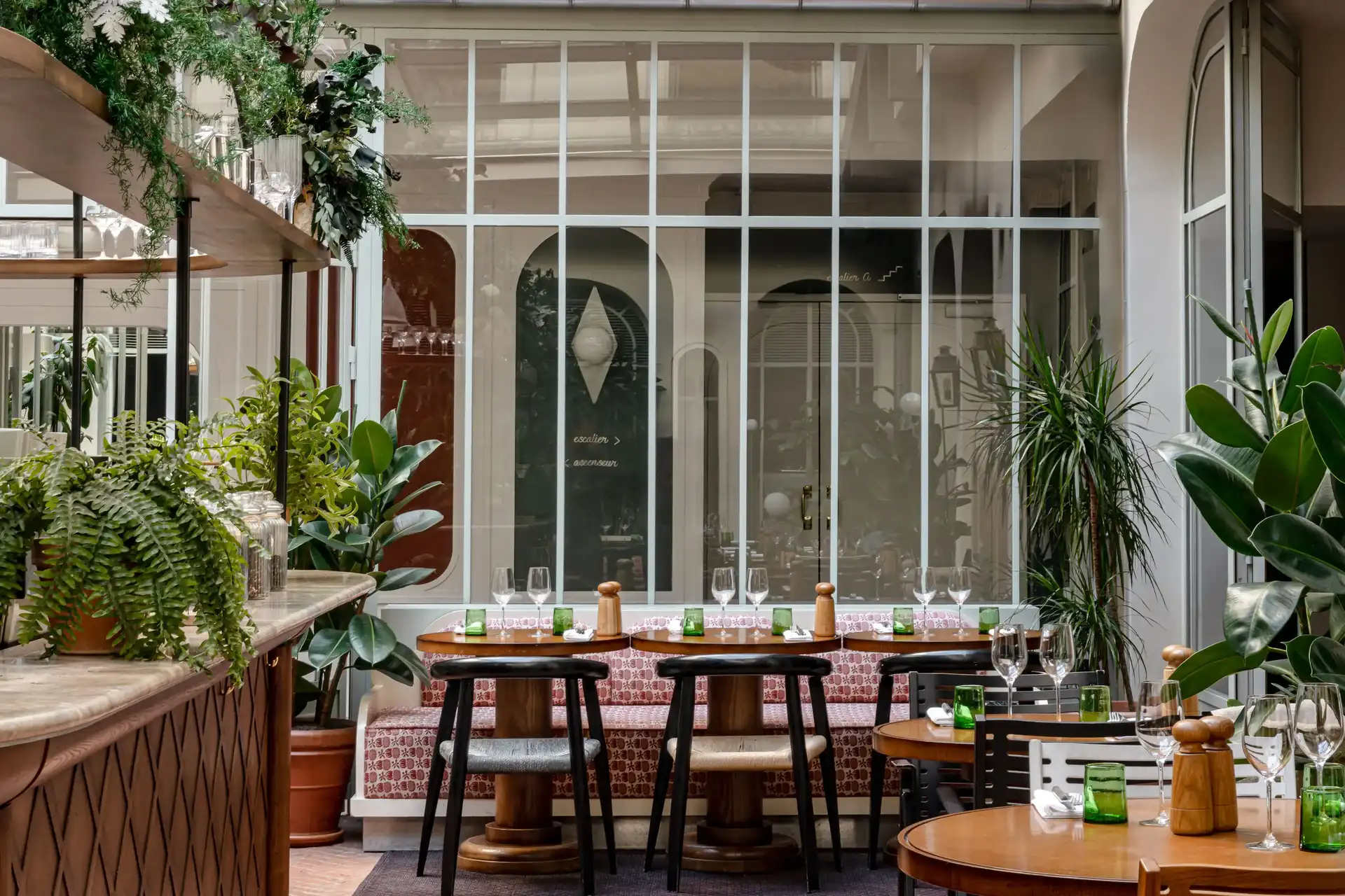Accogliente interno del ristorante con tavoli in legno, sedie, panca a motivi geometrici e piante verdi lussureggianti.