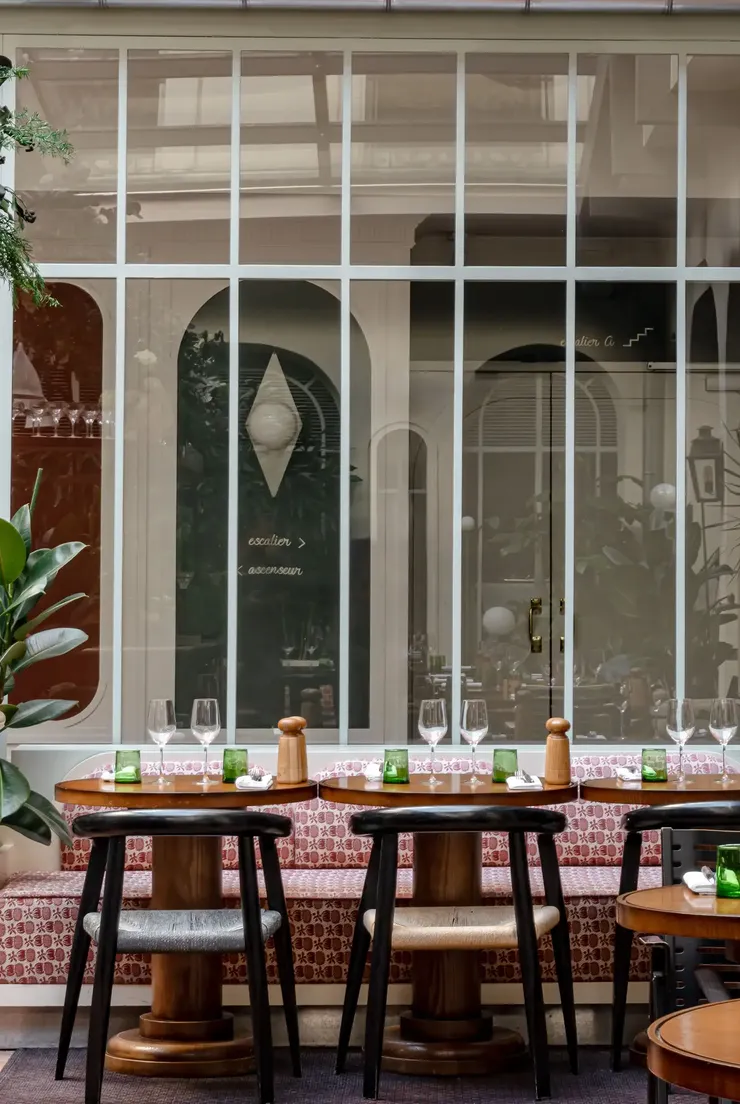 Accoglienti posti a sedere al ristorante con tavoli in legno, sedie nere, bicchieri e una panca decorata con ampie finestre.
