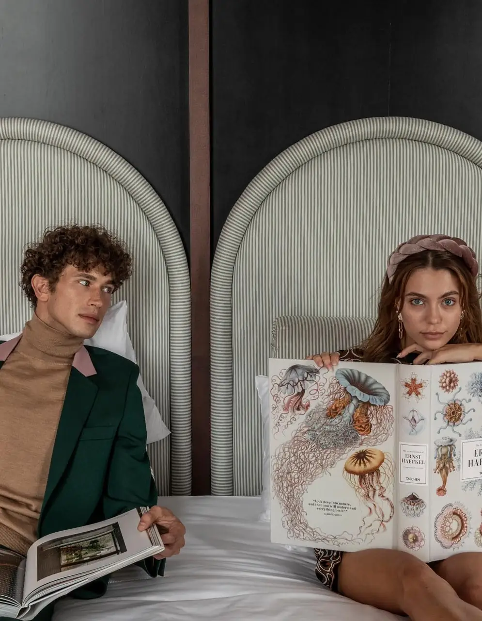 Man and woman sitting on a bed reading large illustrated books, with the woman showing jellyfish drawings.