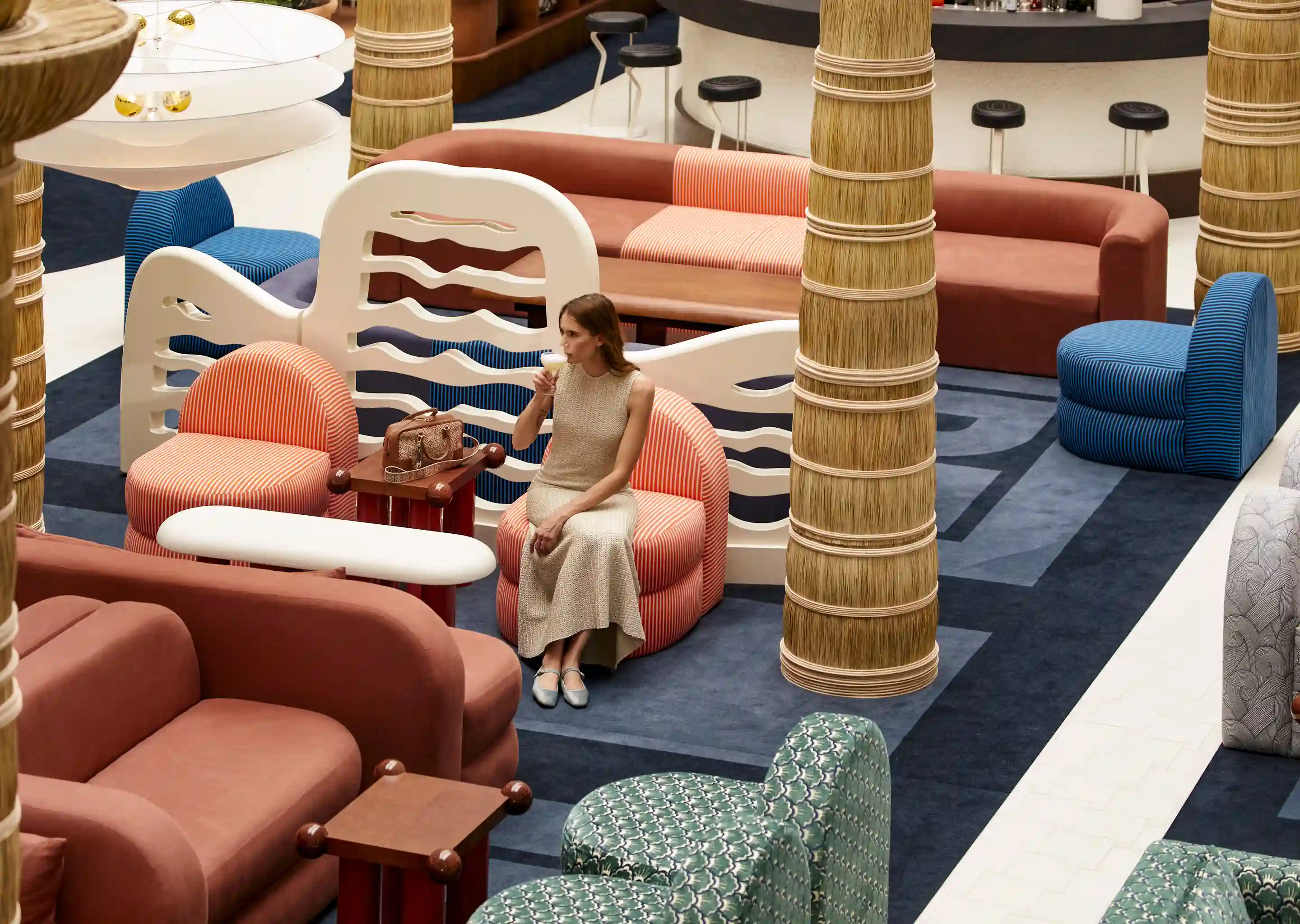 Mujer vestida de color beige sentada en una silla naranja en un salón moderno con sofás estampados de colores.