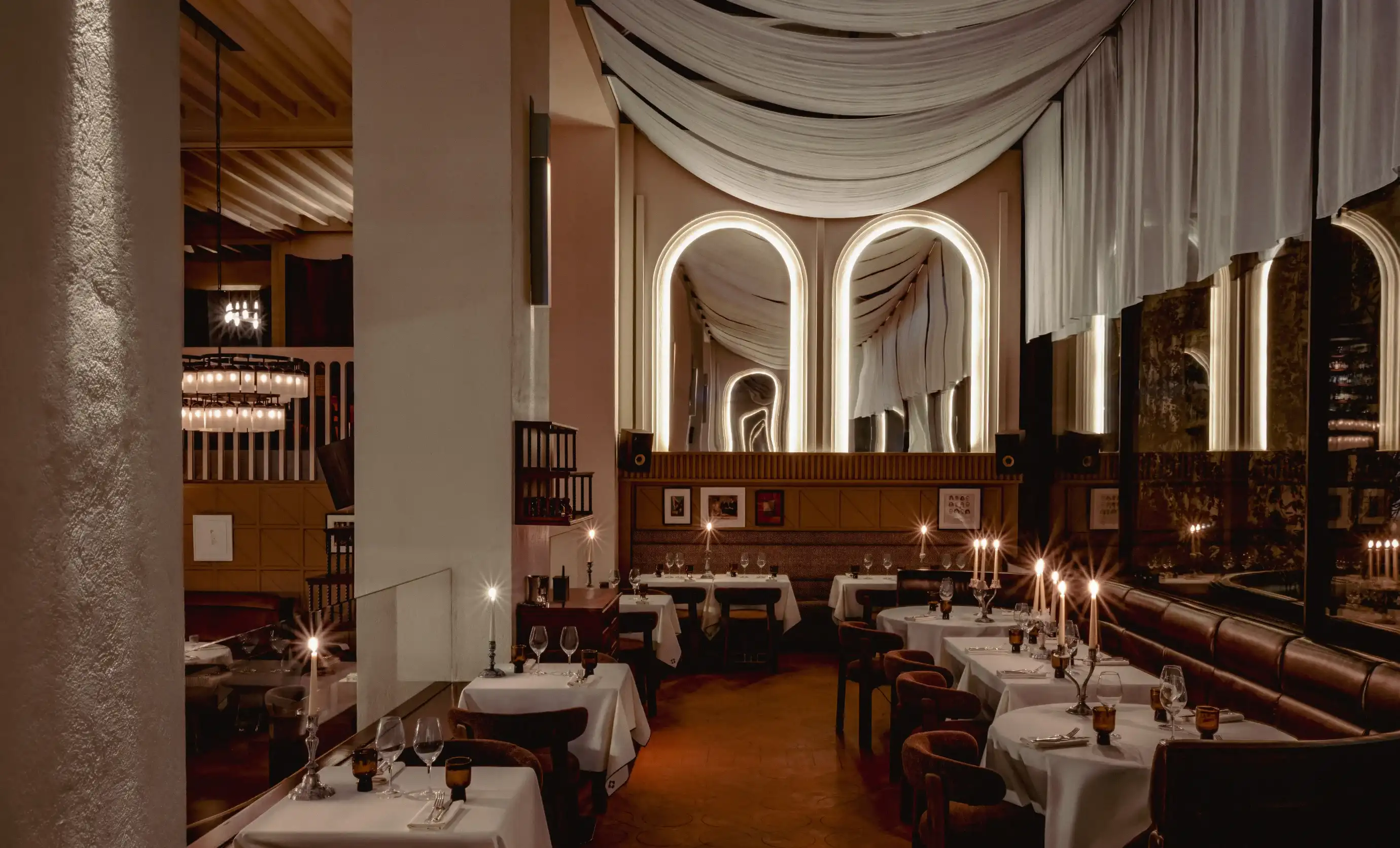 Elegante ristorante poco illuminato con tovaglie bianche, candele, archi e morbidi drappeggi del soffitto in tessuto.