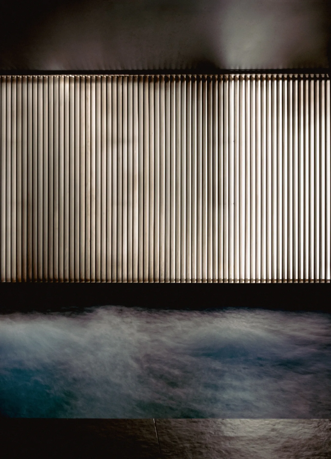 Piscina termale coperta con acqua gorgogliante davanti a una parete a doghe di legno illuminata.