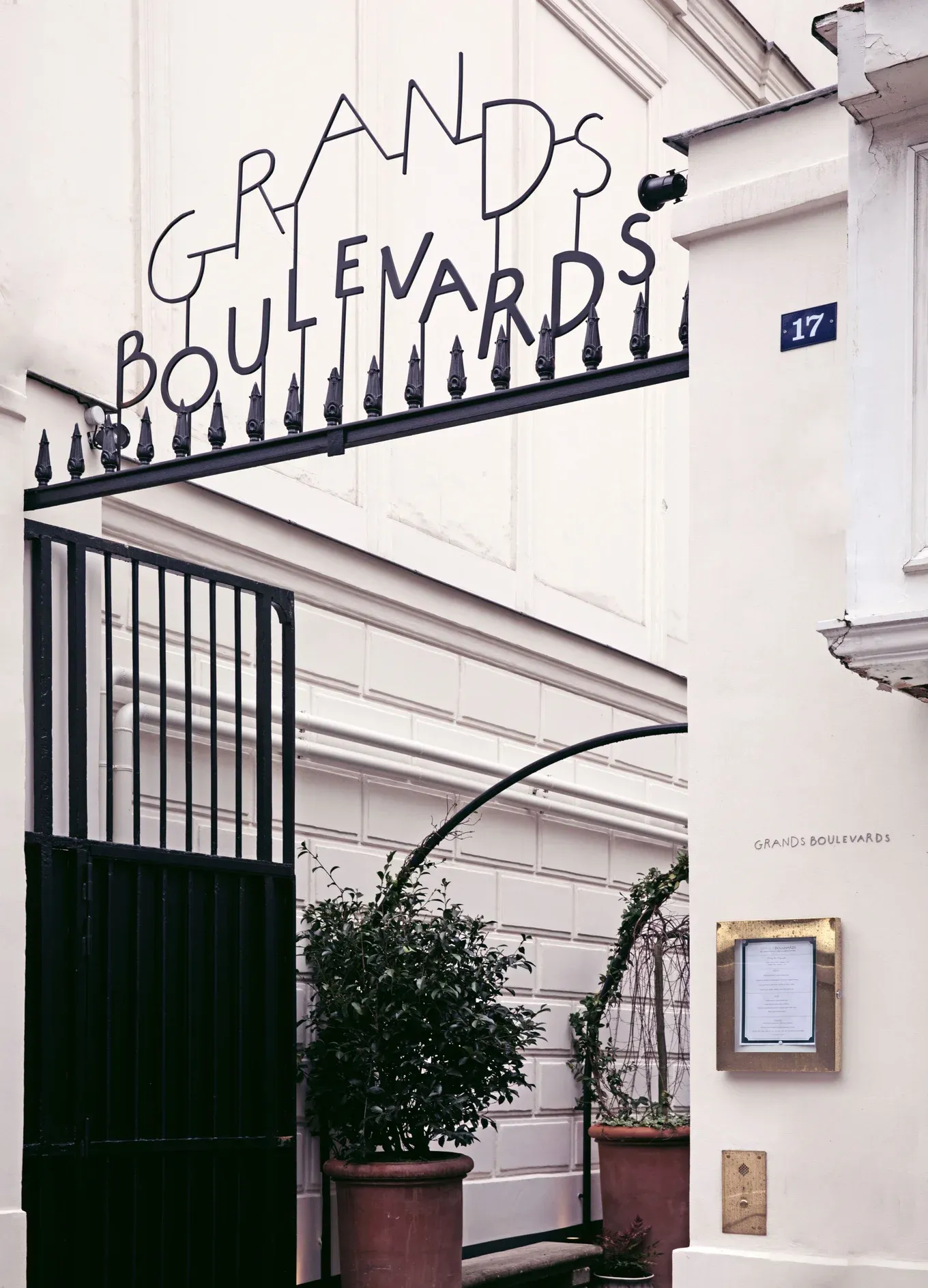 Portão de entrada de metal preto com placa de Grands Boulevards acima e vasos de plantas dentro.