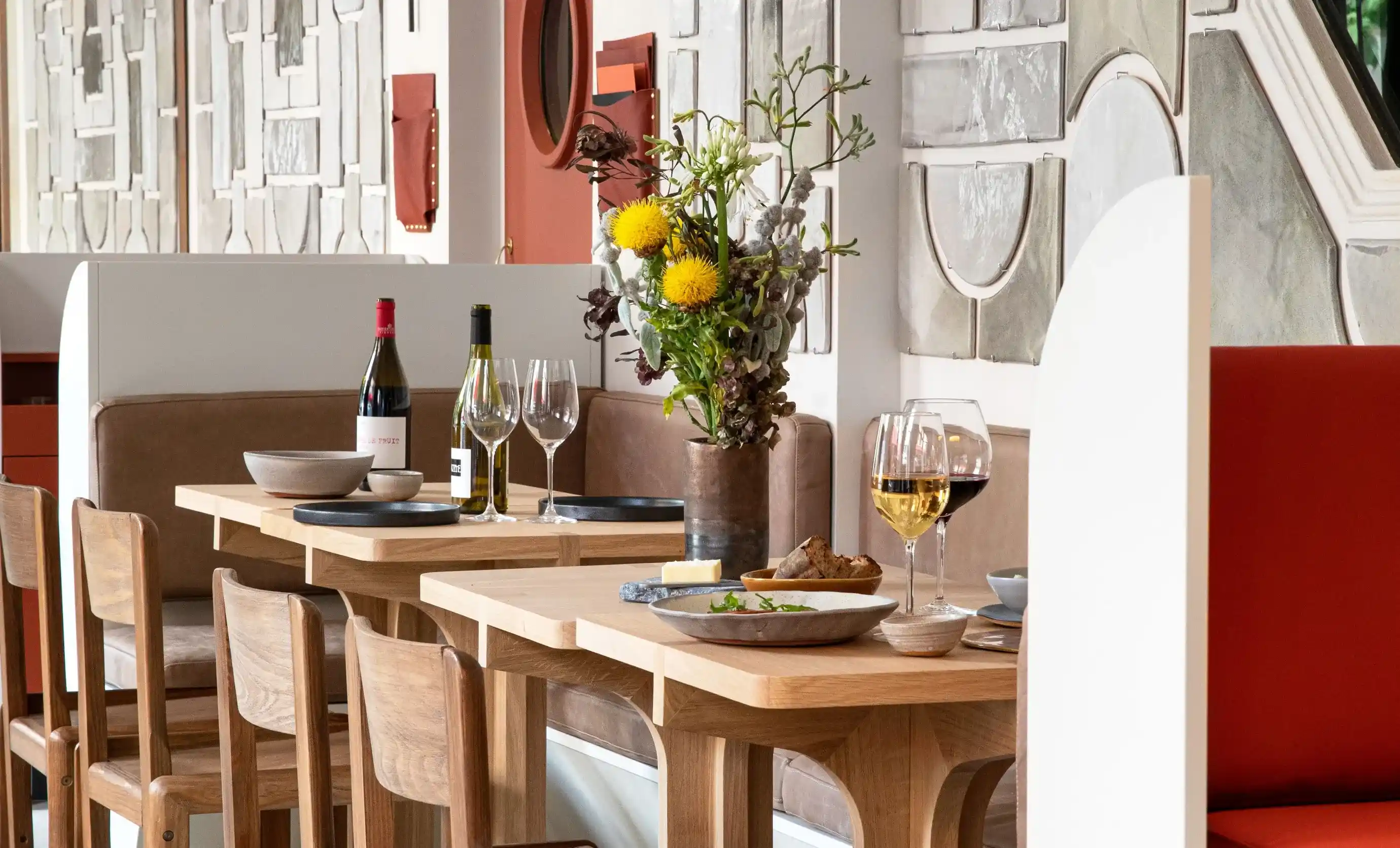 Mesa de restaurante moderna com garrafas de vinho, copos, tigelas, pão e uma peça central de flores.