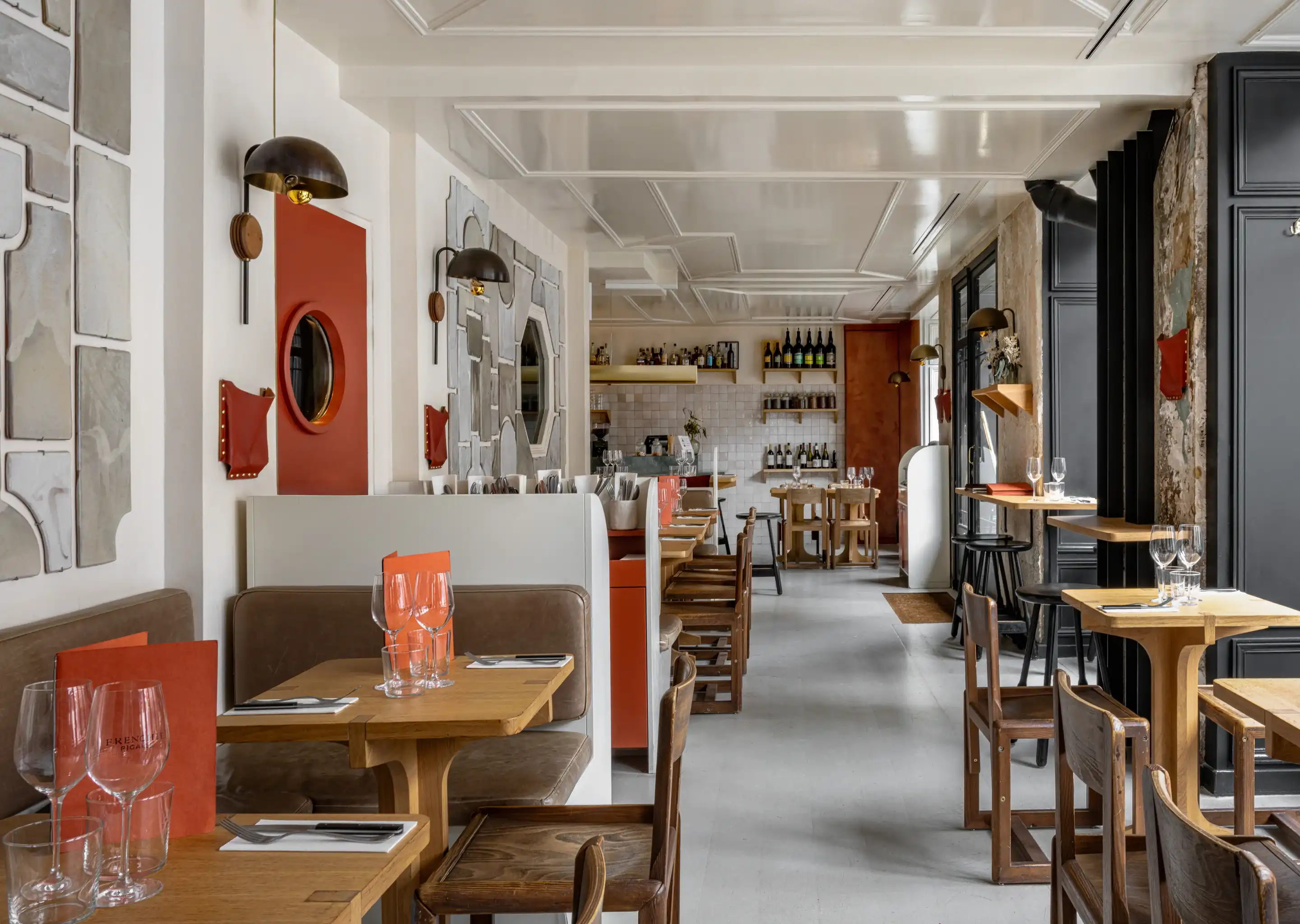 Interior aconchegante do restaurante com mesas de madeira, cadeiras marrons, paredes brancas e luminárias modernas.