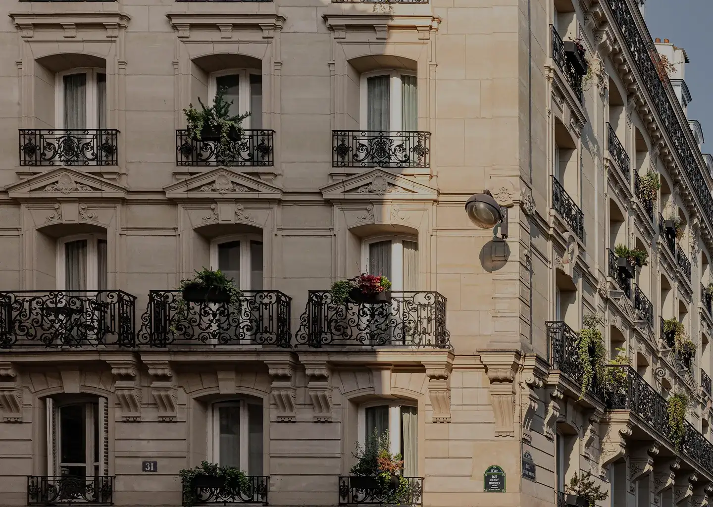 Fachada de edifício parisiense com varandas ornamentadas e floreiras com luz natural.