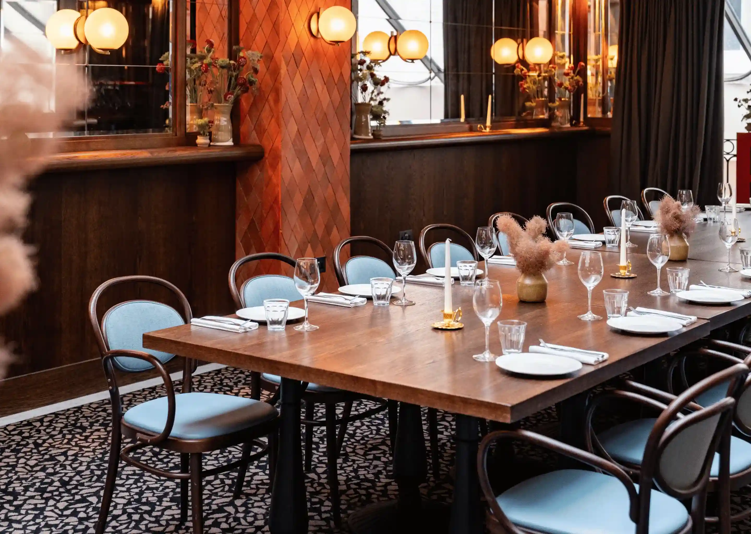 Elegante tavolo da pranzo da ristorante con piatti, bicchieri, candele e centrotavola floreali su moquette a motivi geometrici.