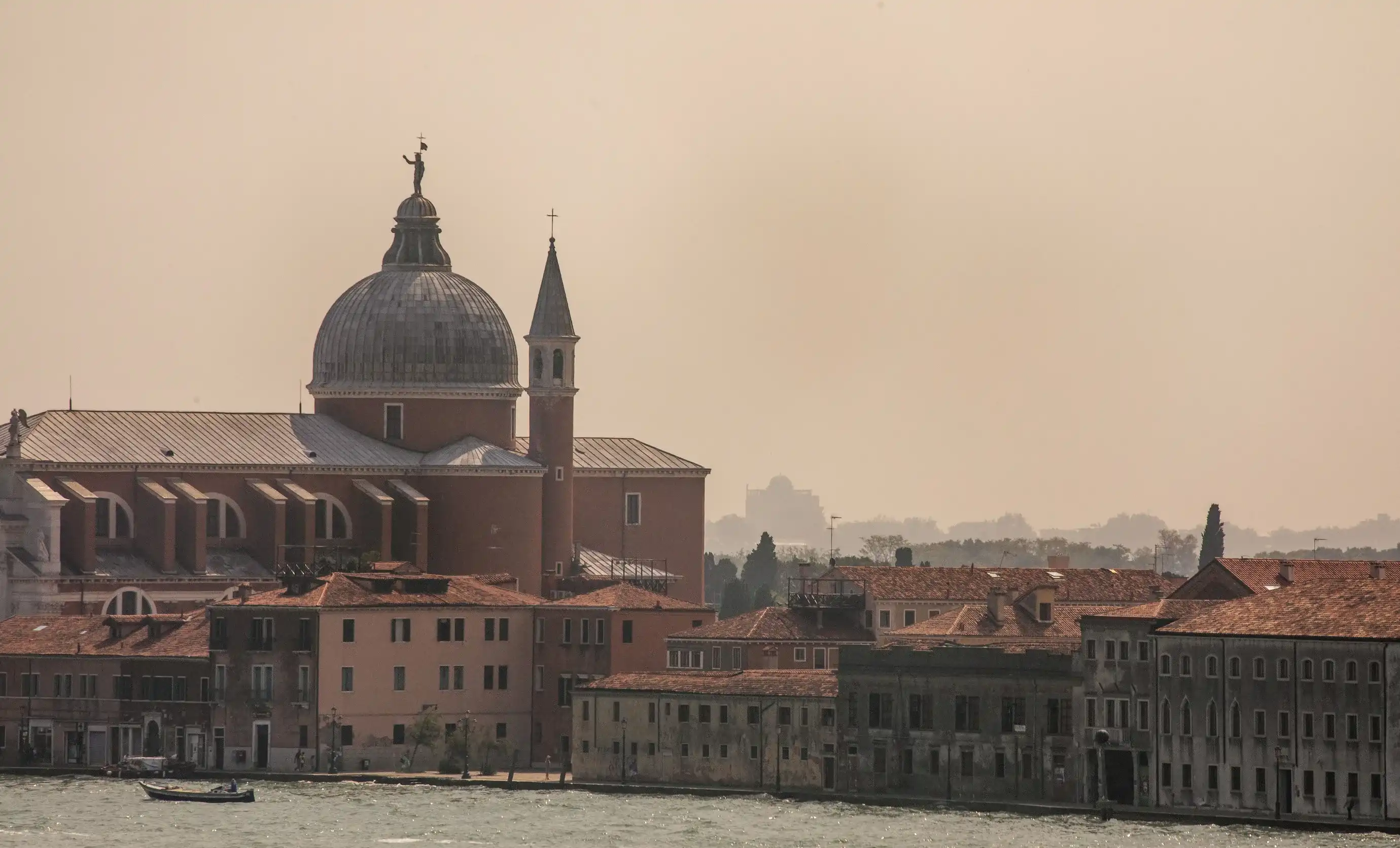 Edifícios históricos à beira-mar com uma grande igreja abobadada e torre sineira sob um céu nebuloso.