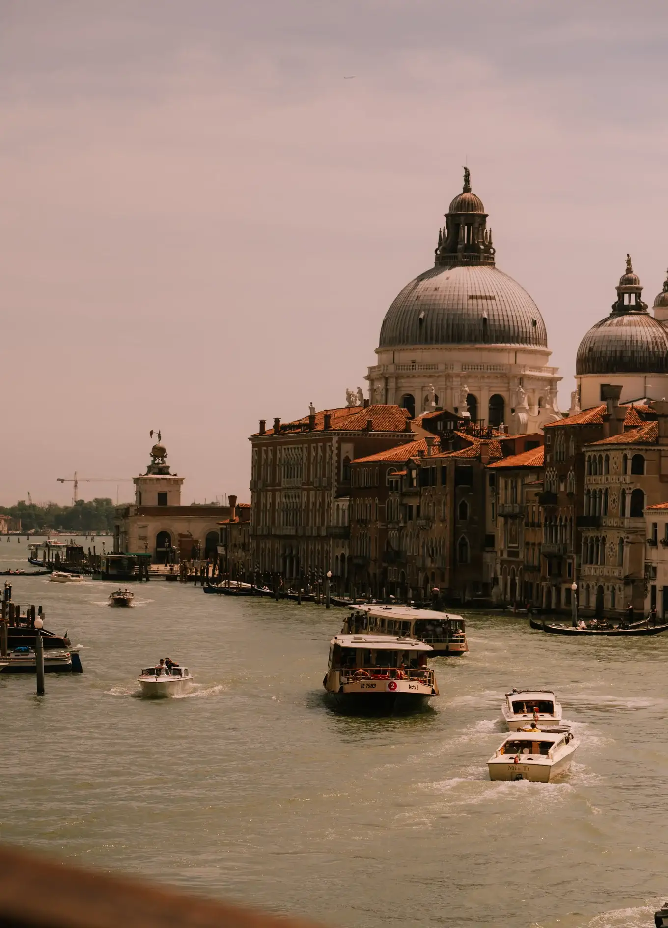 Barcos navegando por um canal em Veneza com edifícios históricos e igreja abobadada ao fundo.