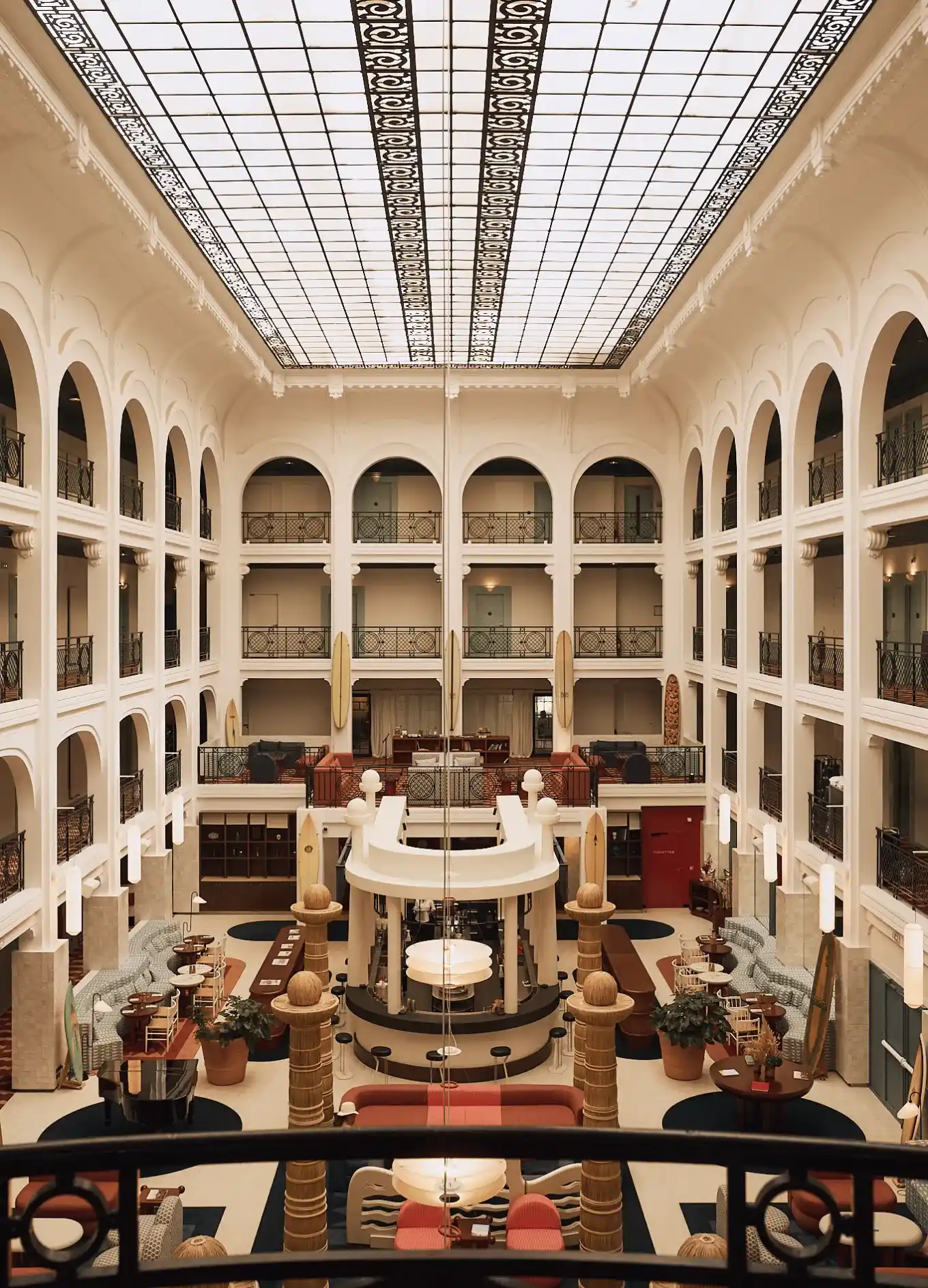 Spaziosa hall dell'hotel con balconi ad arco, posti a sedere, colonne e un grande soffitto in vetro.