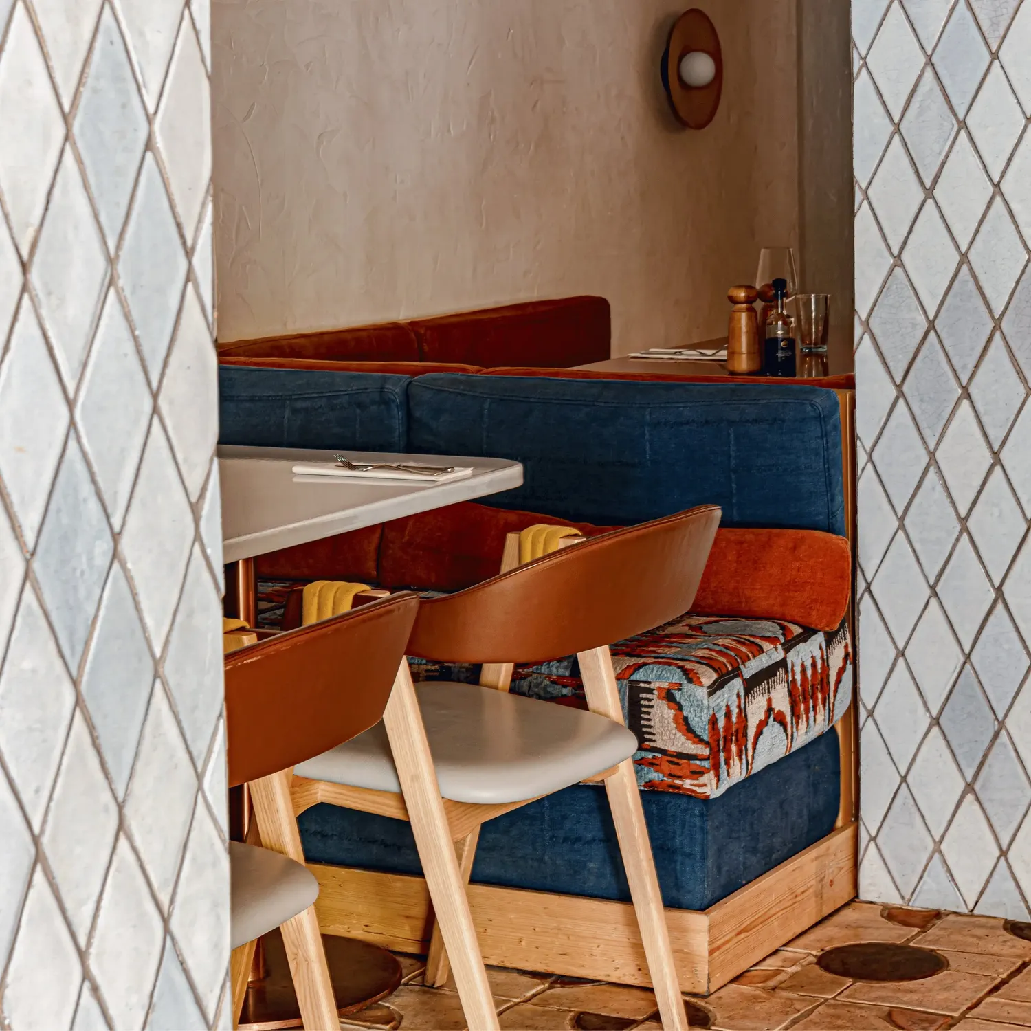 Restaurante aconchegante com banco almofadado estampado, cadeiras de madeira e mesa branca.