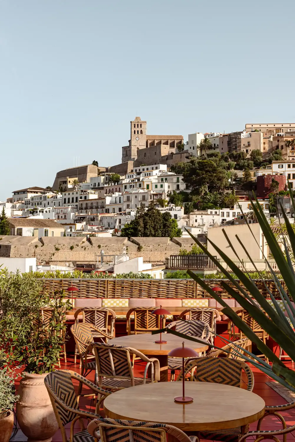Assentos de restaurante ao ar livre com cadeiras e mesas de vime com vista para edifícios na encosta e uma torre do relógio.